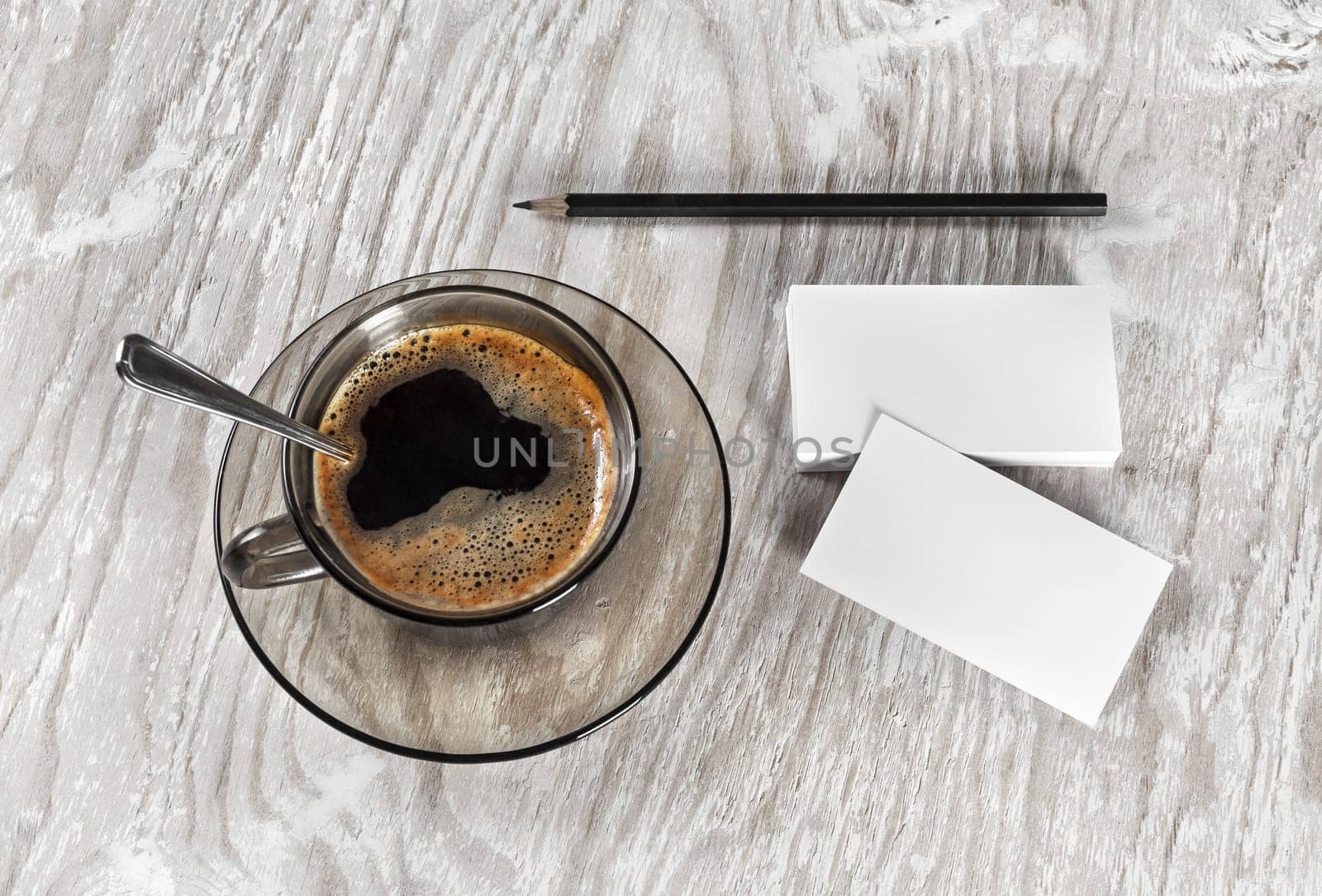 Coffee cup, business cards and a pencil on light wooden table background. Blank objects for placing your design. Top view.