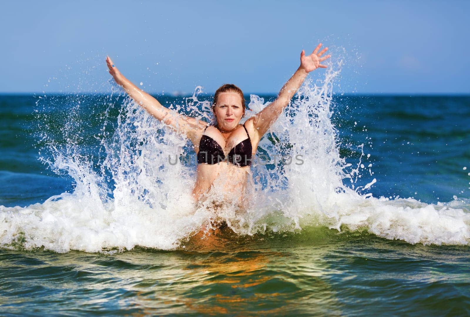 Beautiful girl on a background of blue sea with waves and clear sky on a sunny day. Sexy woman in bikini enjoying a dip in the sea wave.