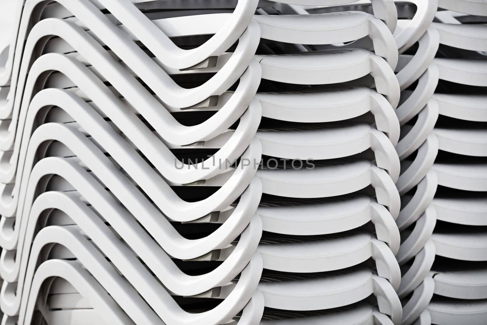 Folded stack of white plastic deck chairs. Pile of beach loungers. Abstract background or texture