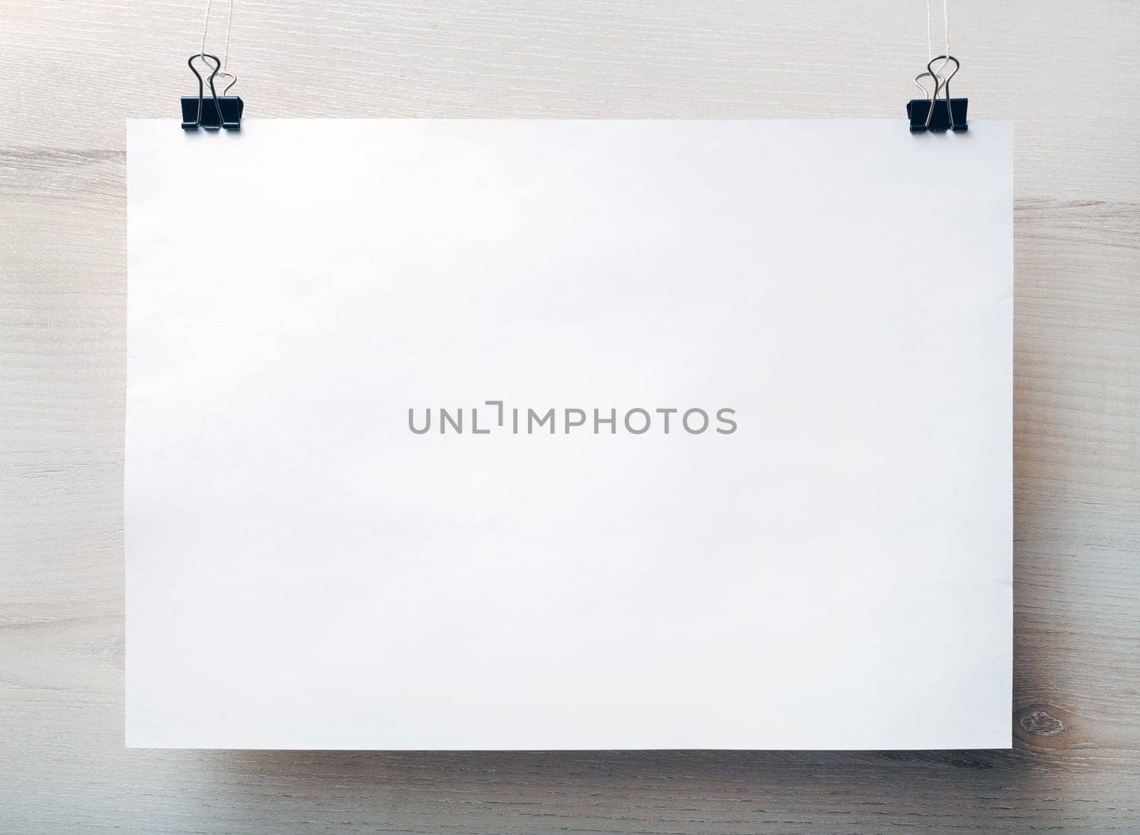 Blank white paper poster hanging on light wooden background. Blank template for placing your design. Front view.