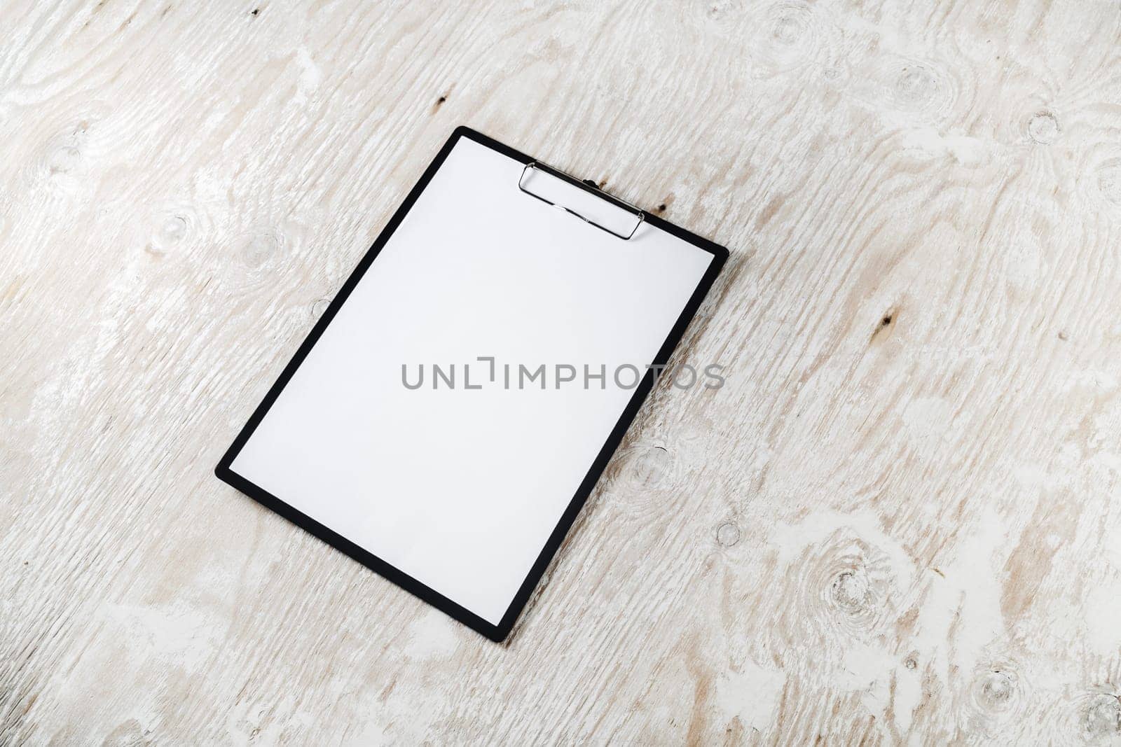Photo of clipboard with a blank sheet of paper on light wooden background with plenty of copy space. Blank template for design presentations and portfolios. Mock-up for branding identity.