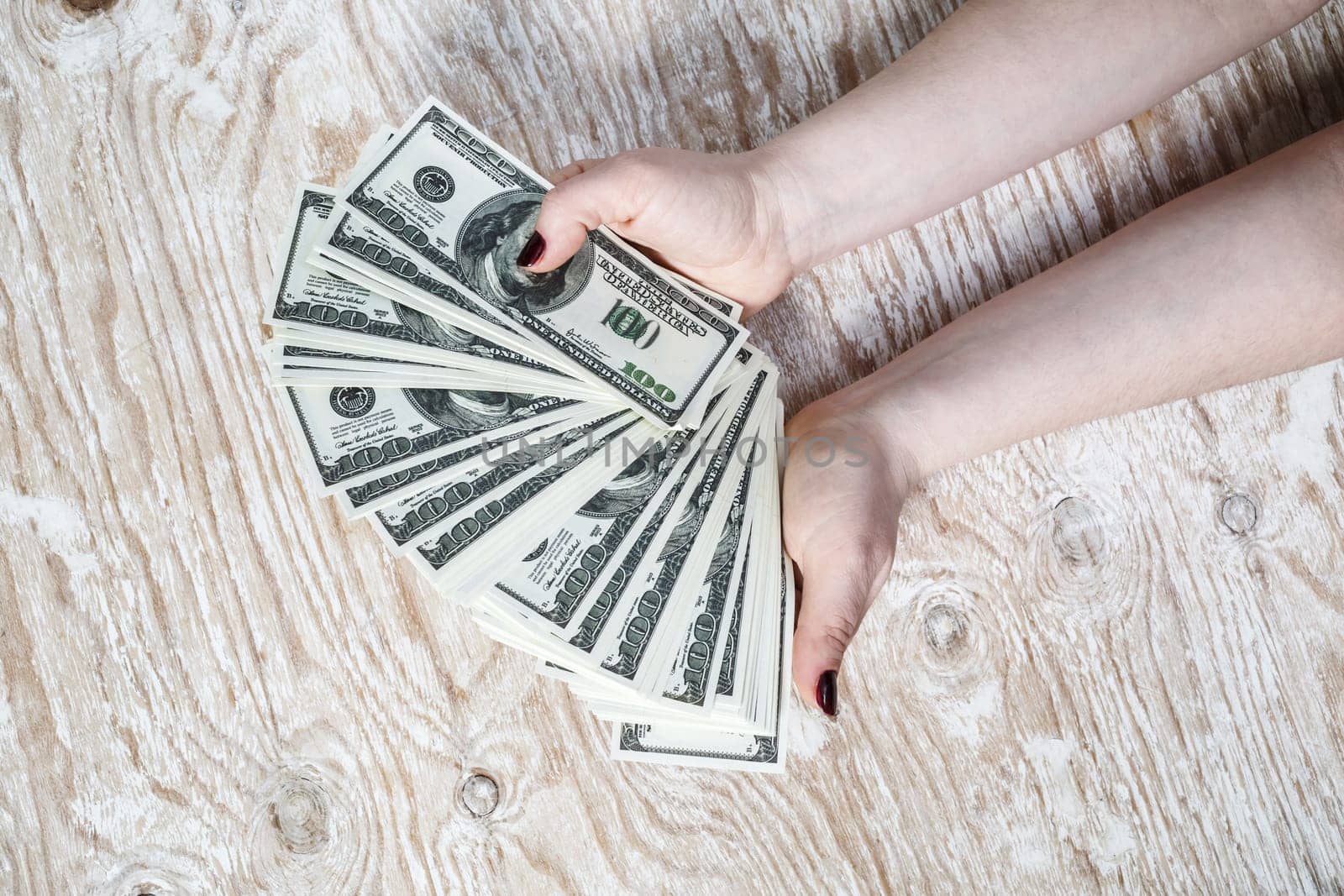 Dollar banknotes in hands. Woman hands counting dollar banknotes on light wooden background.