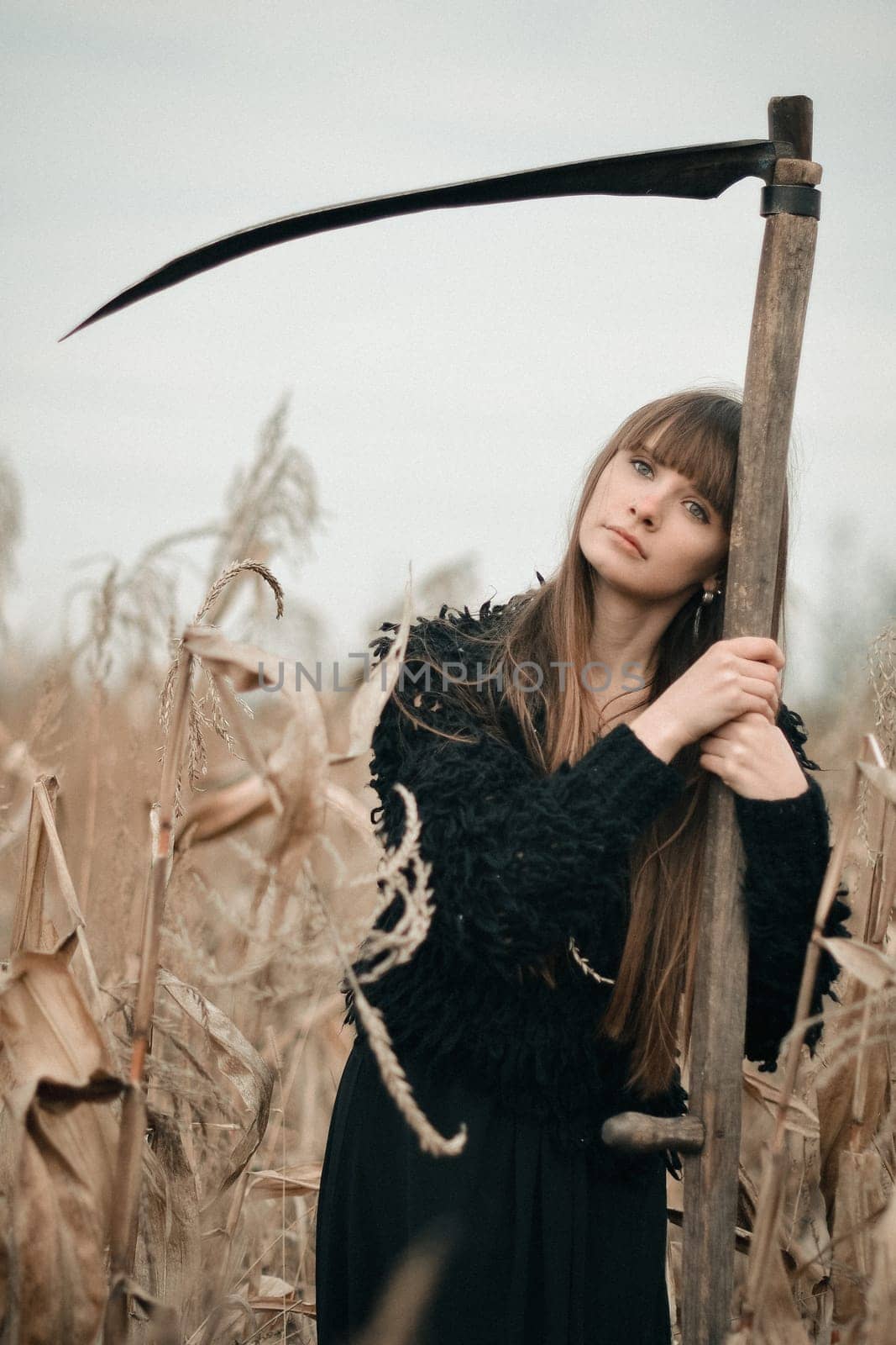 Thinking girl with scythe standing in autumn fiels wih wheat