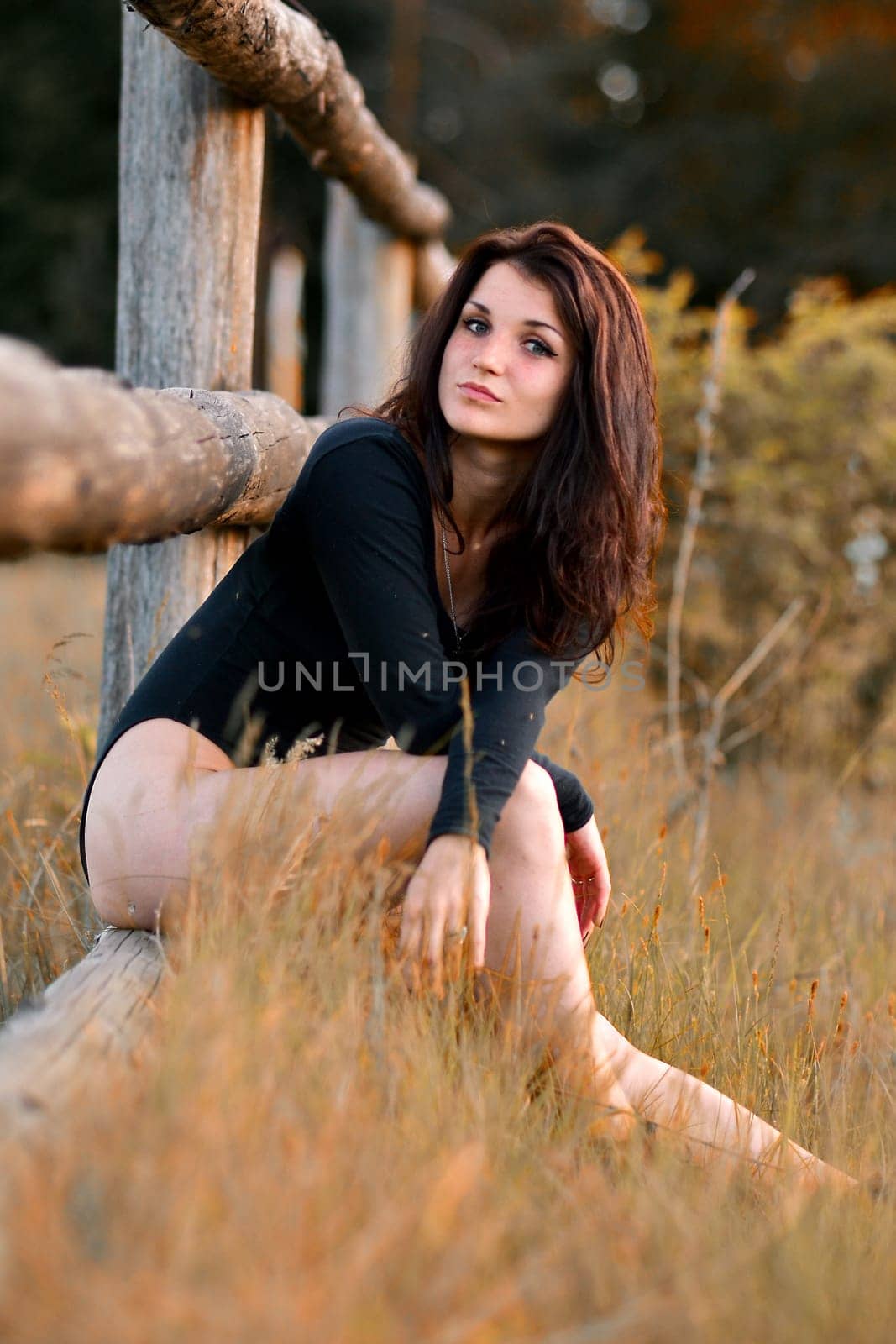 Sexy,sexual,very beautiful attractive girl sitting on the wooden fence in nice,red,green,yellow field,garden,forest with amazing view.Sunset.Nice girl in summer,autumn forest.Beautiful girl on fence.Relax on the wooden fence.
