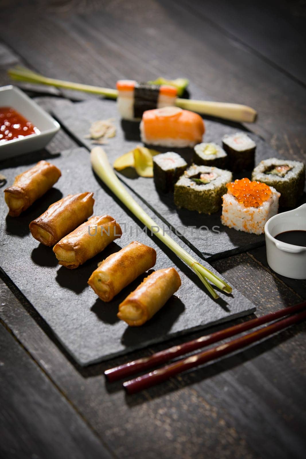 Spring rolls and sushi on black wooden table