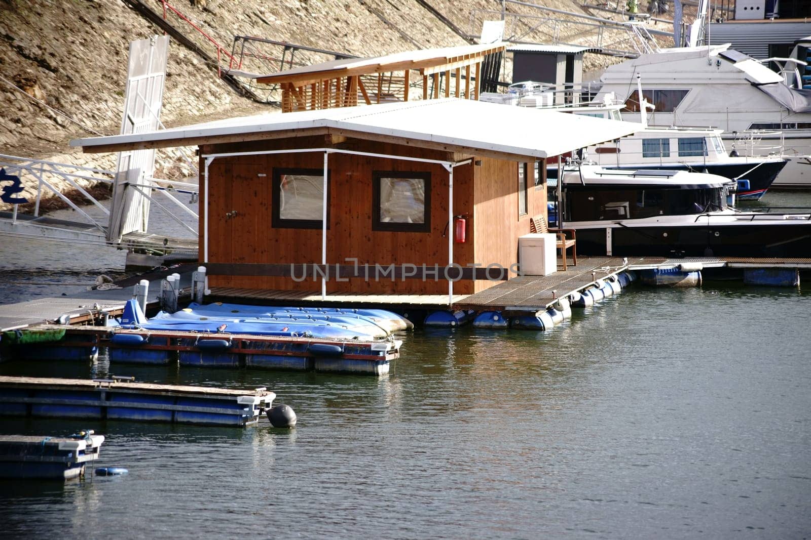 A small wooden houseboat as well as yachts and motor boats anchor in an inland port on the river Rhine.