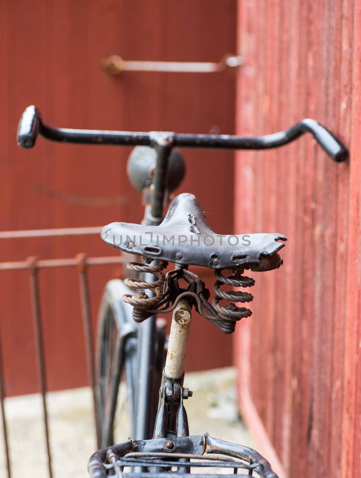 old retro antique black men's bicycle parked up of red wooden fence photographed from behind