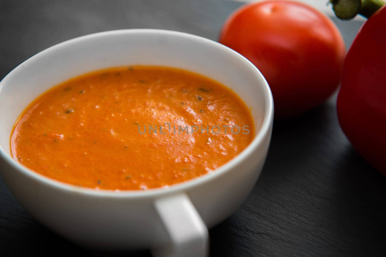 cream soup with roasted peppers and tomatoes on black plate