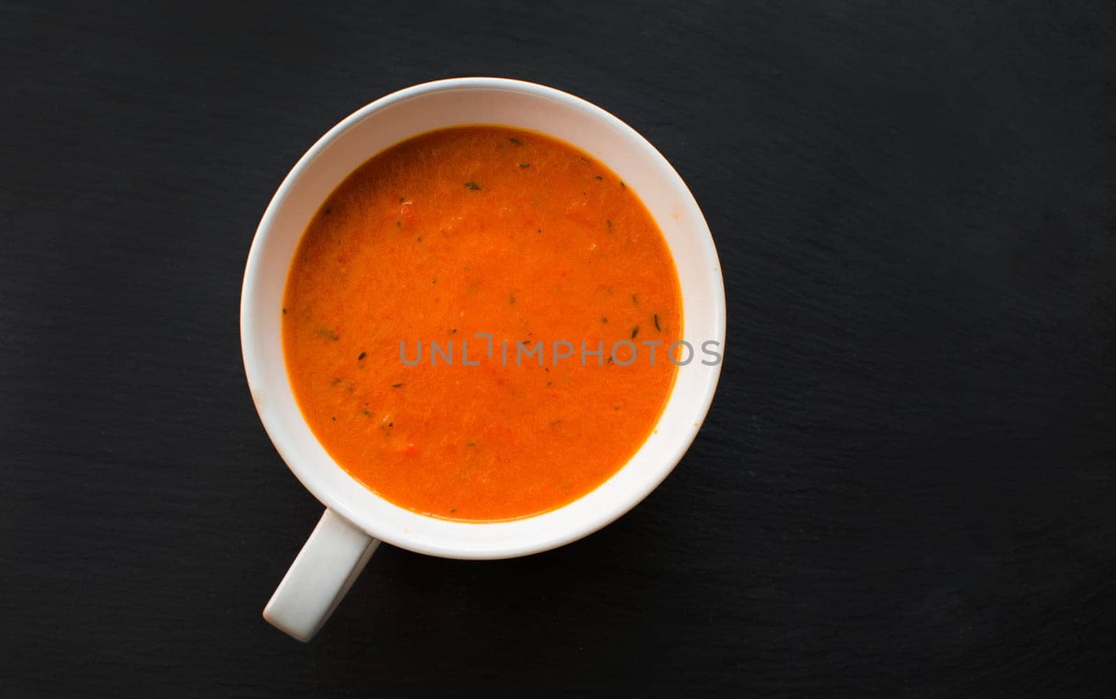 cream soup with roasted peppers and tomatoes on black plate,top view