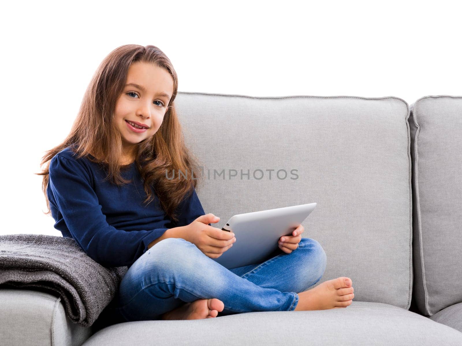 Happy little girl sitting on a couch and working a laptop
