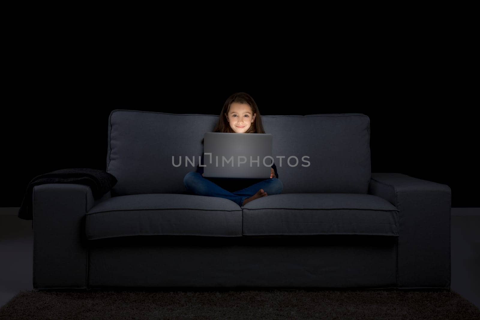 Happy little girl sitting on a couch and working a laptop