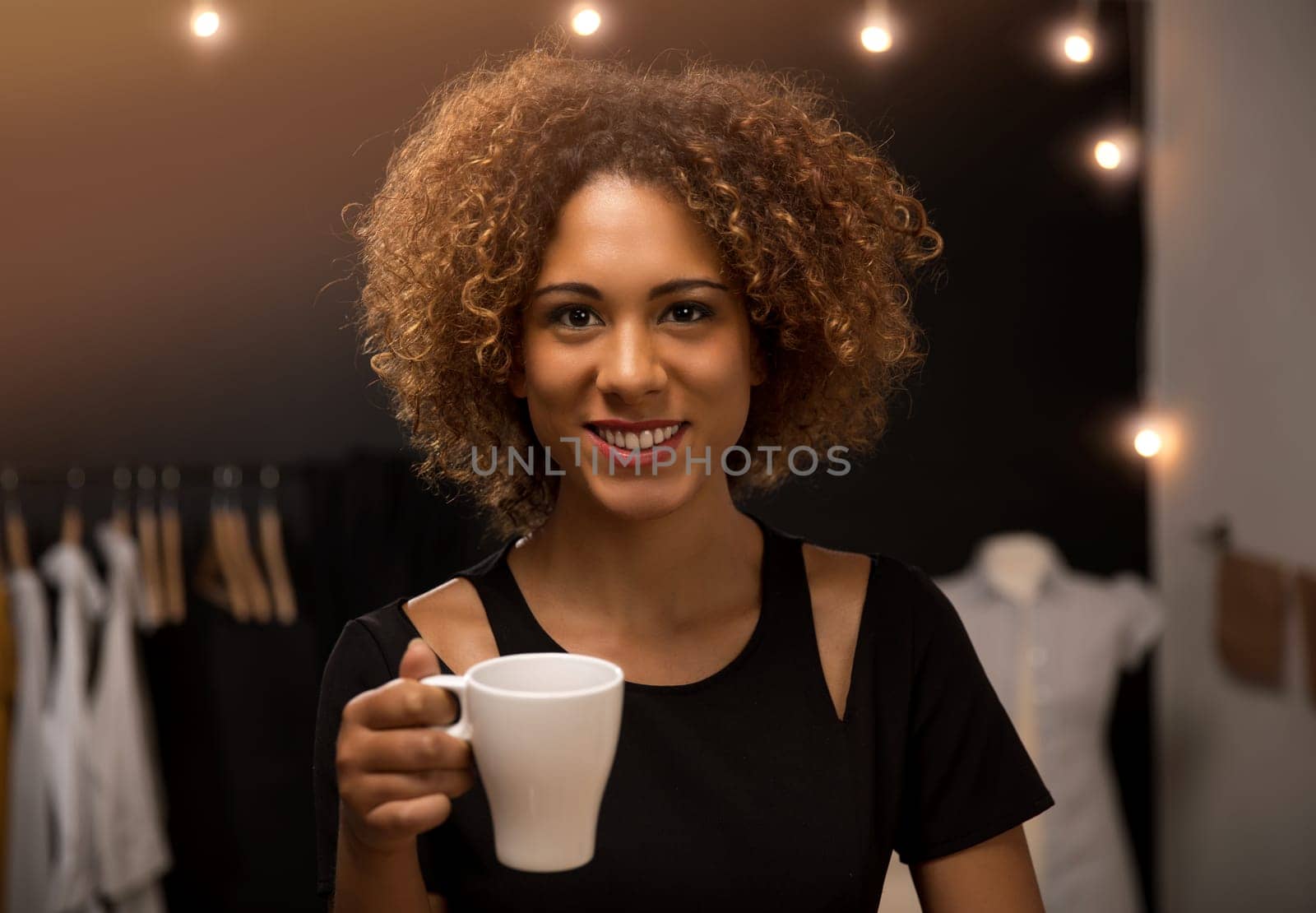 Young fashion designer on her atelier making a pause and drinking coffee