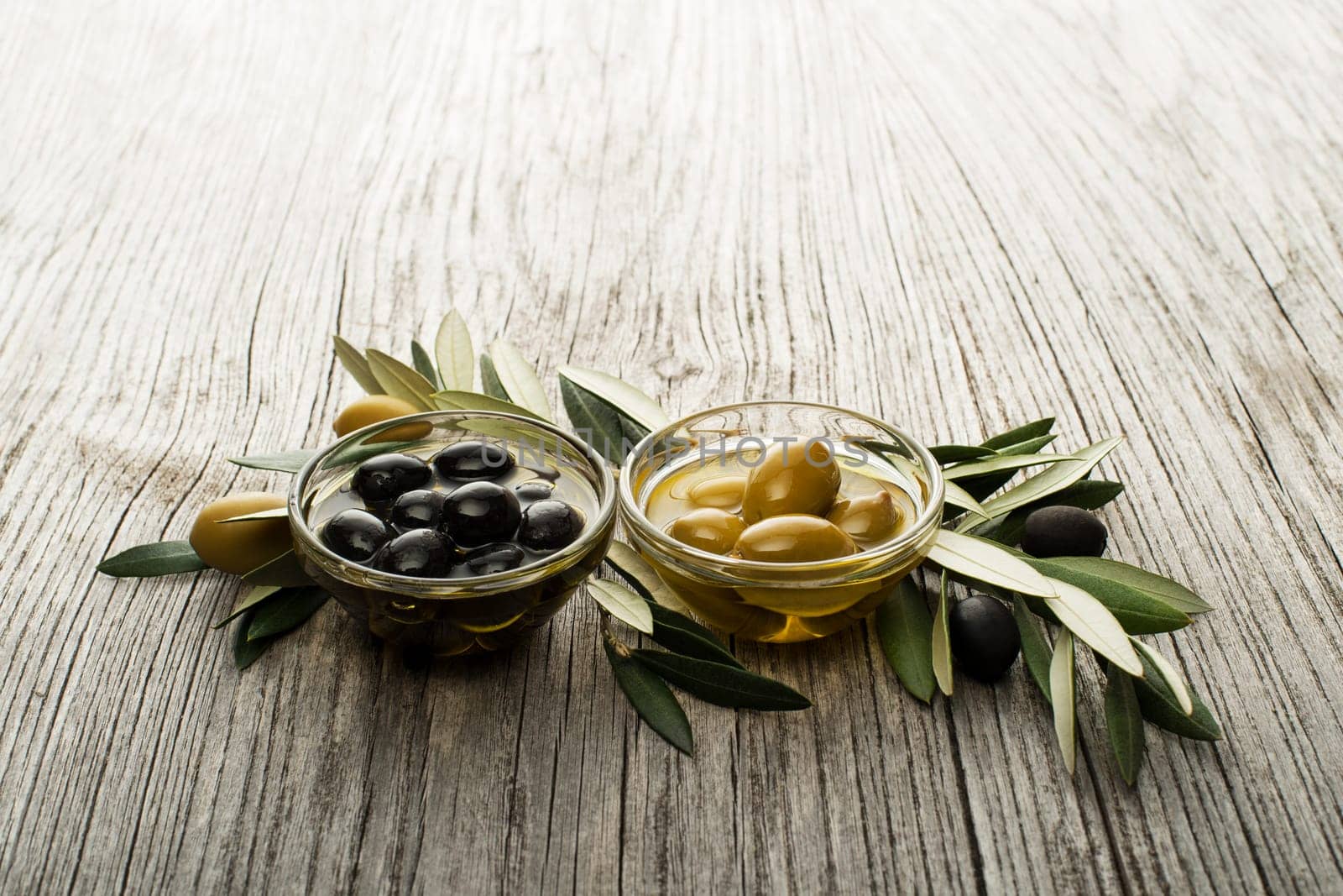 Olive oil with fresh olive fruits on wooden background.