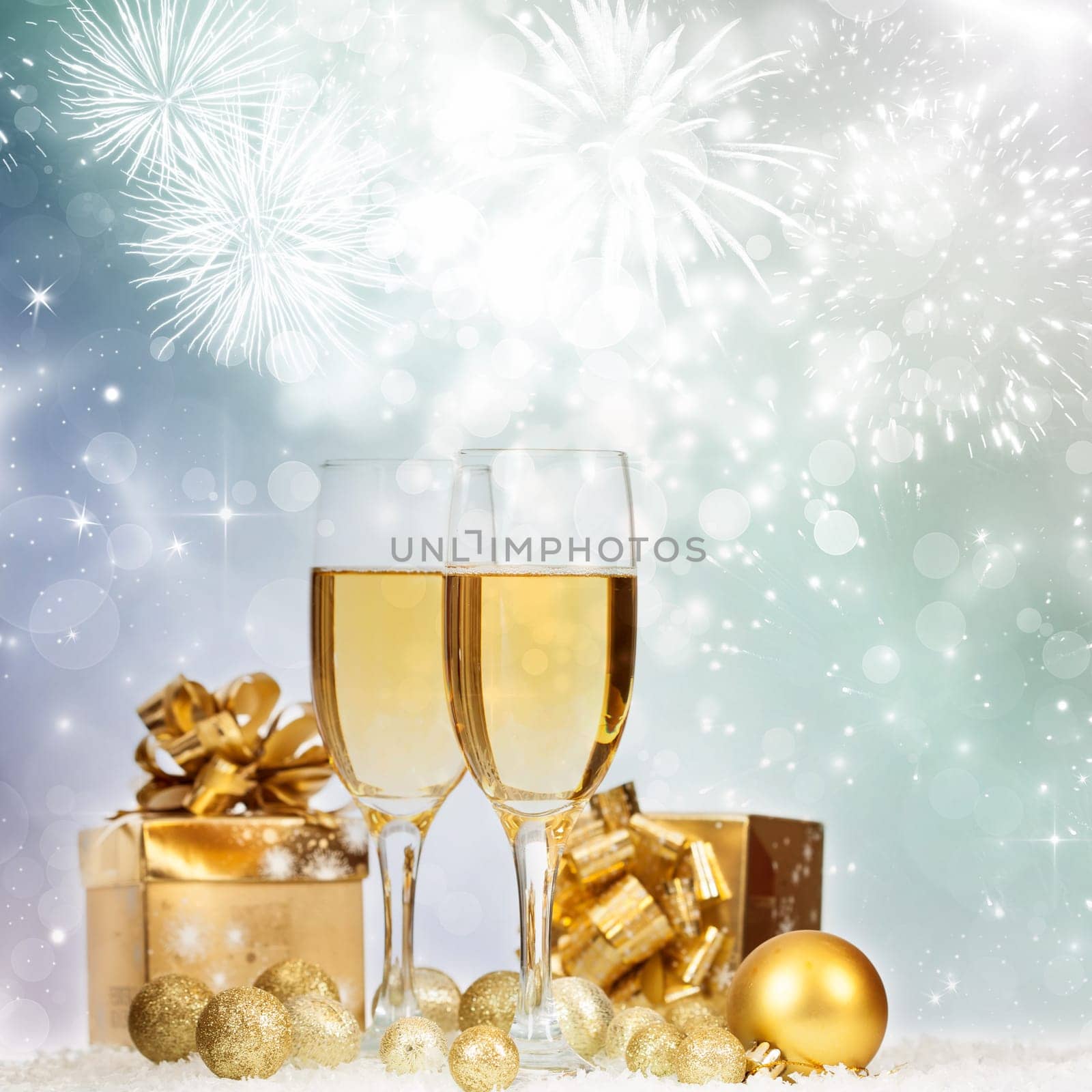 Glasses with champagne and gift box against fireworks and holiday lights