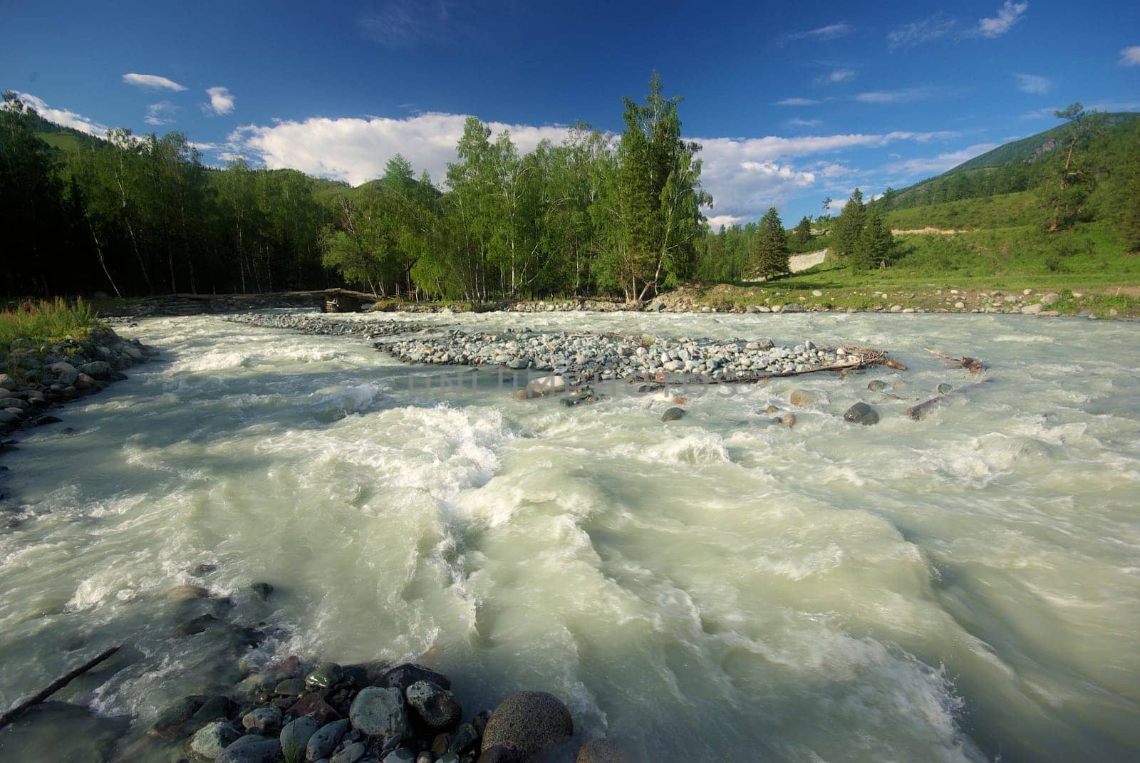 The mountain river in the mountains. Current through the gorge the river. Stones and rocky land near the river. Beautiful mountain landscape.