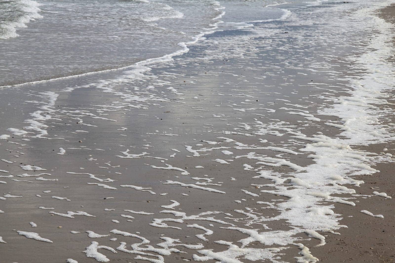 Waves with white foam crowns flood the sandy beach.