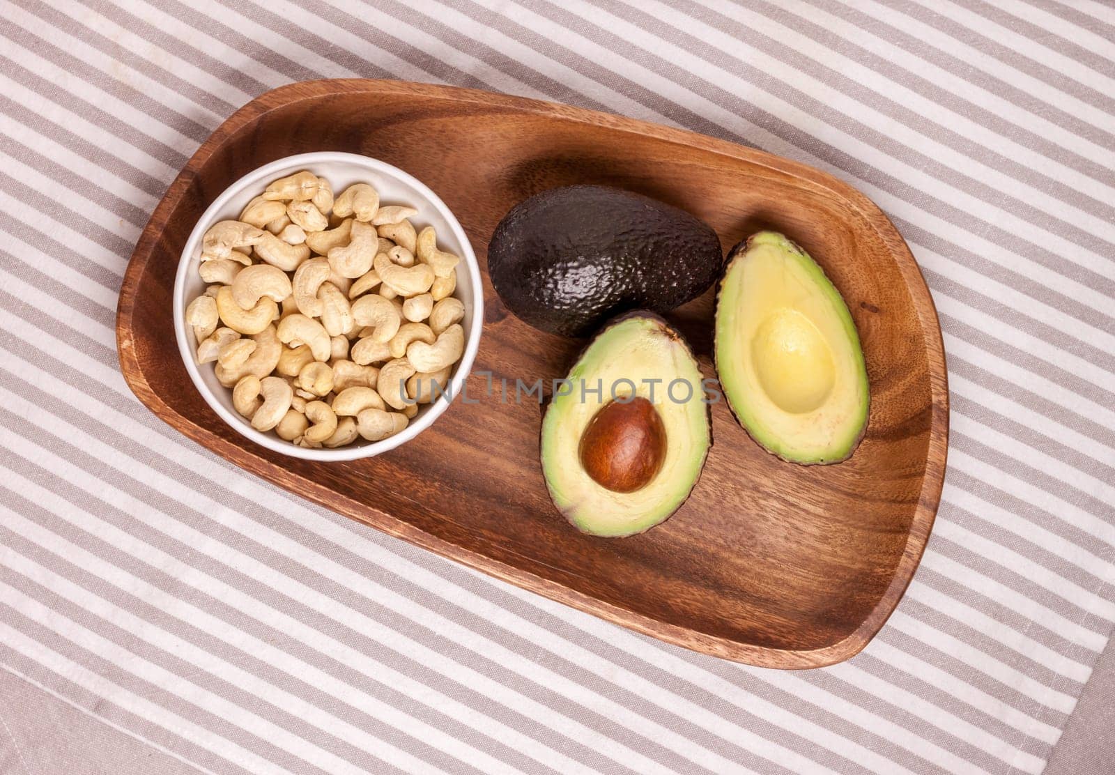 closeup cut avocado and cashew nuts on wooden plate