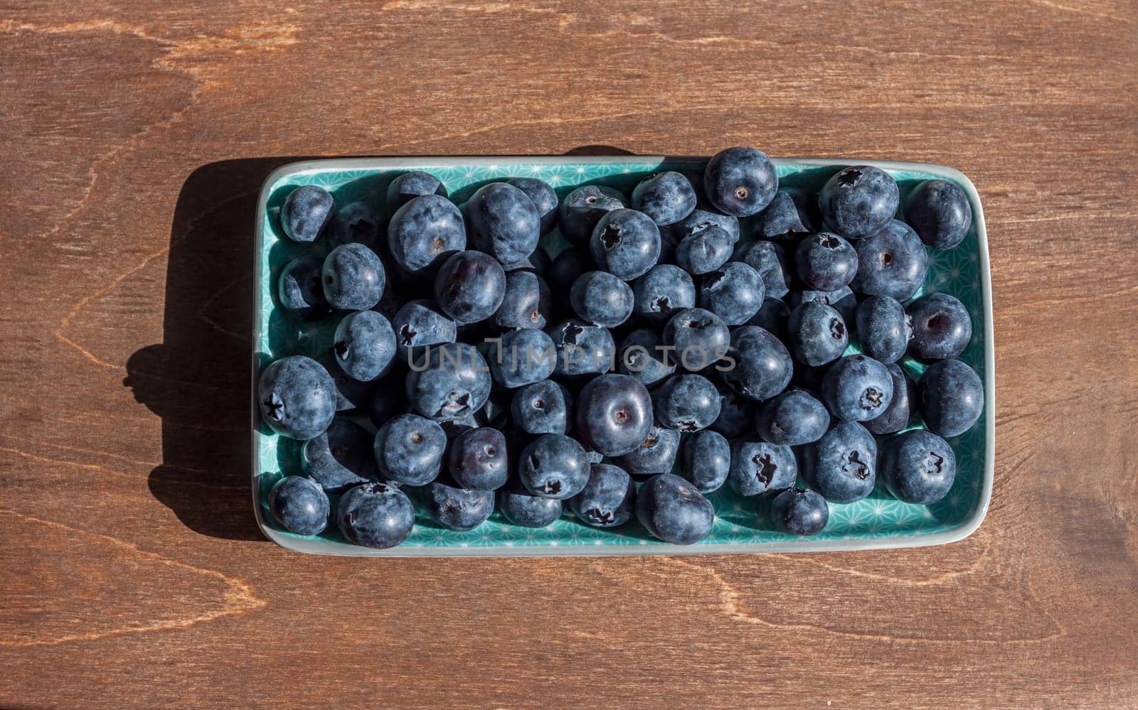 fresh big delicious blueberries in rectangular green plate wooden background
