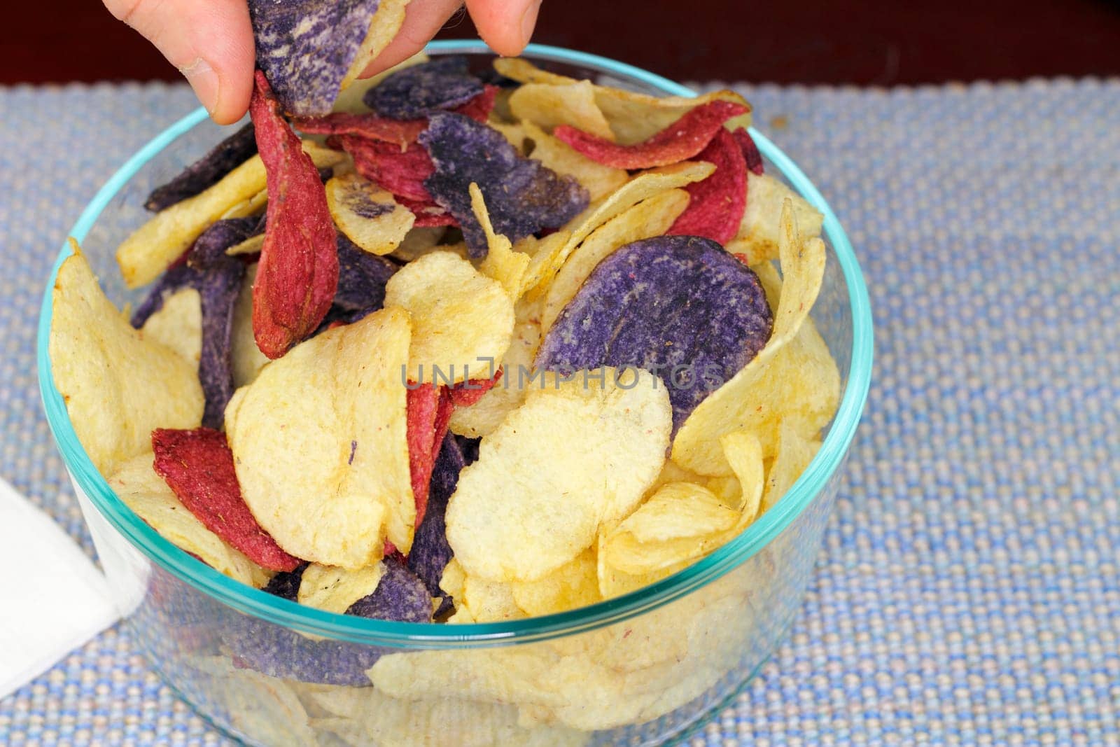 Adult male fingers picking up one of each of three colors of potato chips. Yellow, red and purple potato chips chosen by fingers of an adult male.