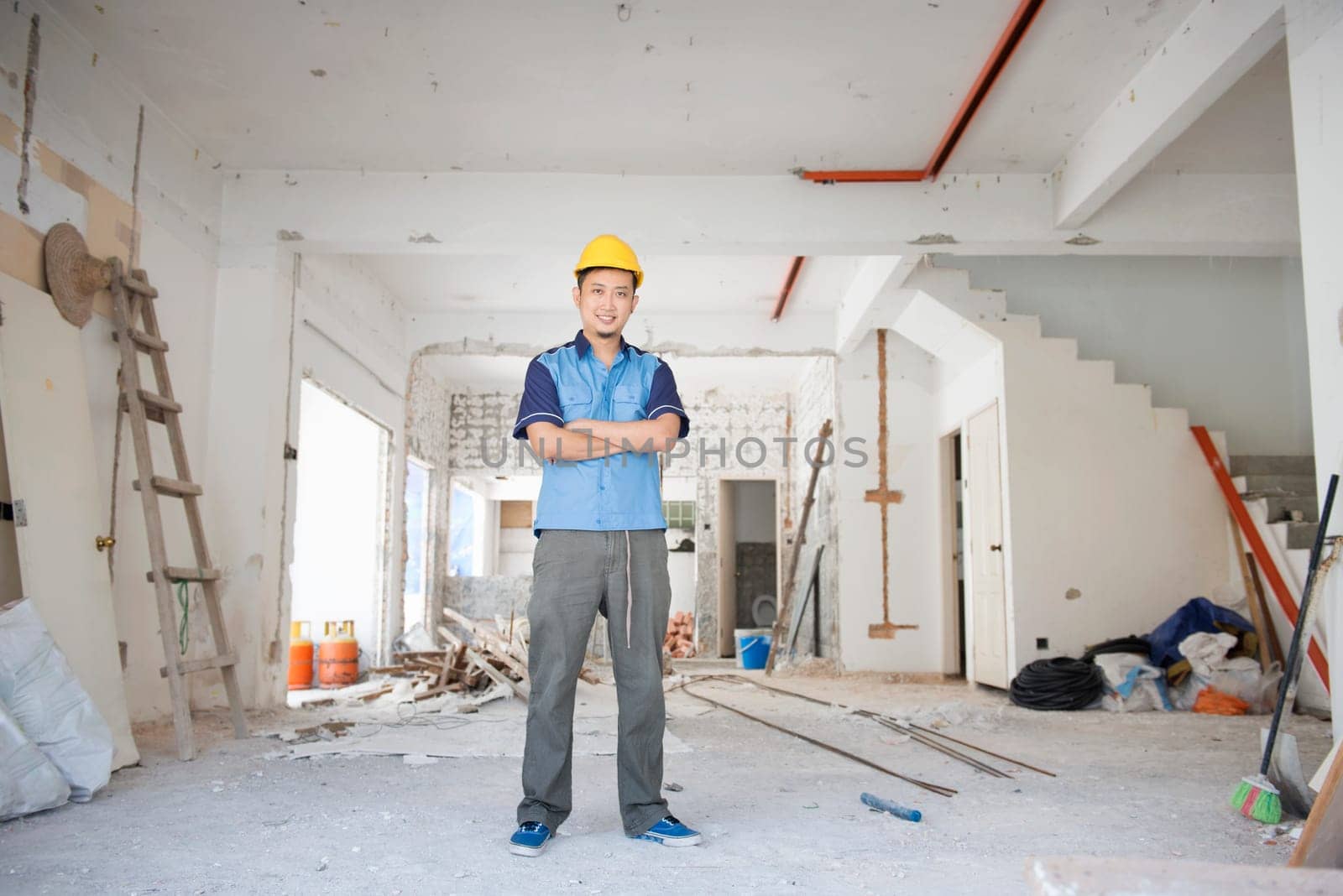 Asian construction worker with hardhat standing at site, house improvement concept.