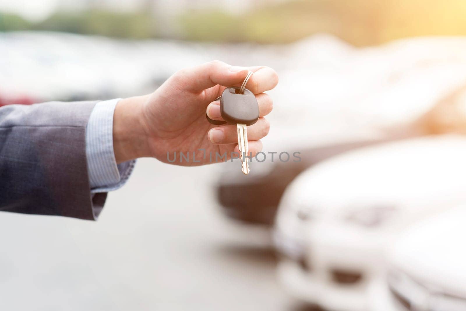 Close up hand holding car key, many automobile at the background.
