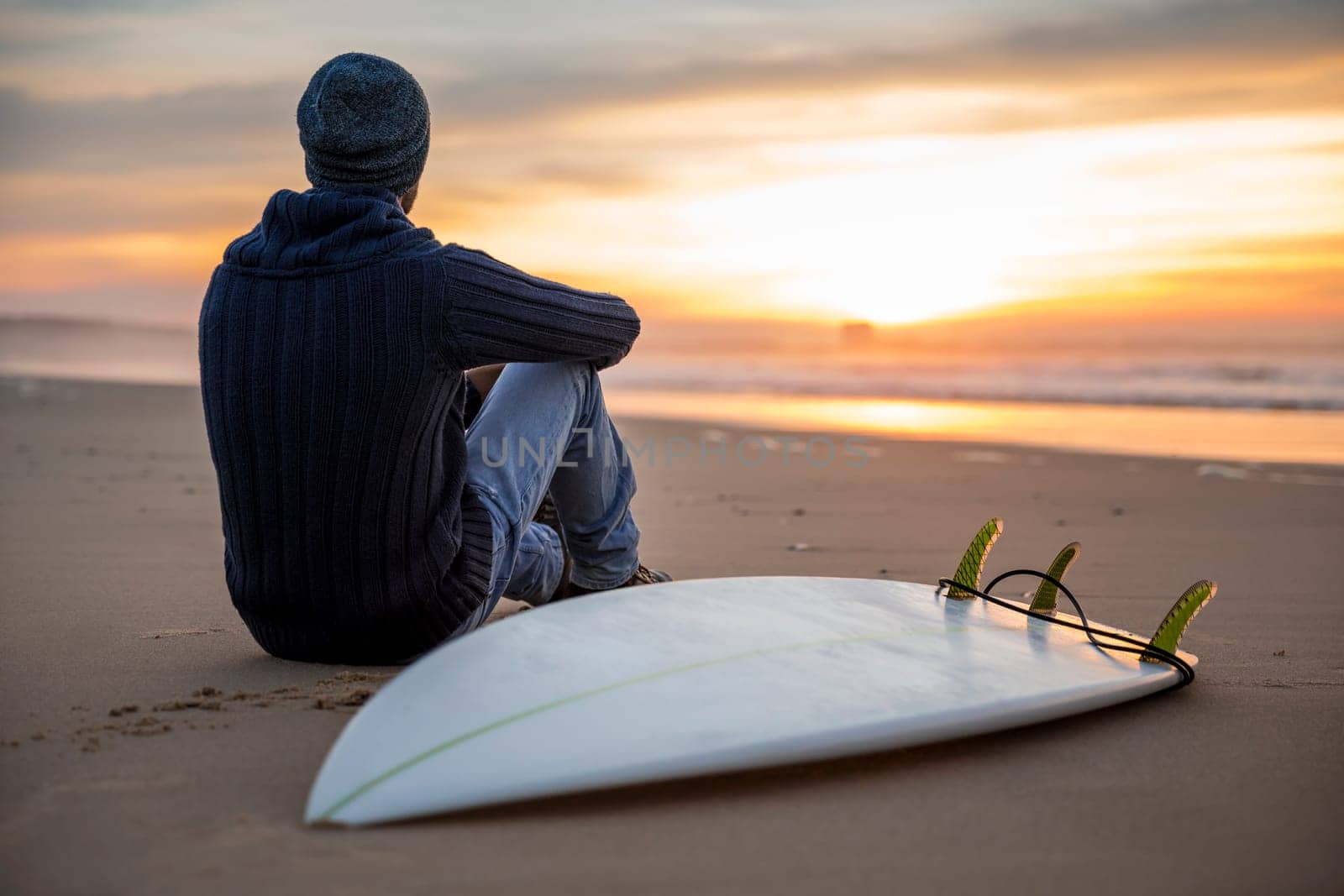 A surfer with his surfboard at the sunset looking to the waves