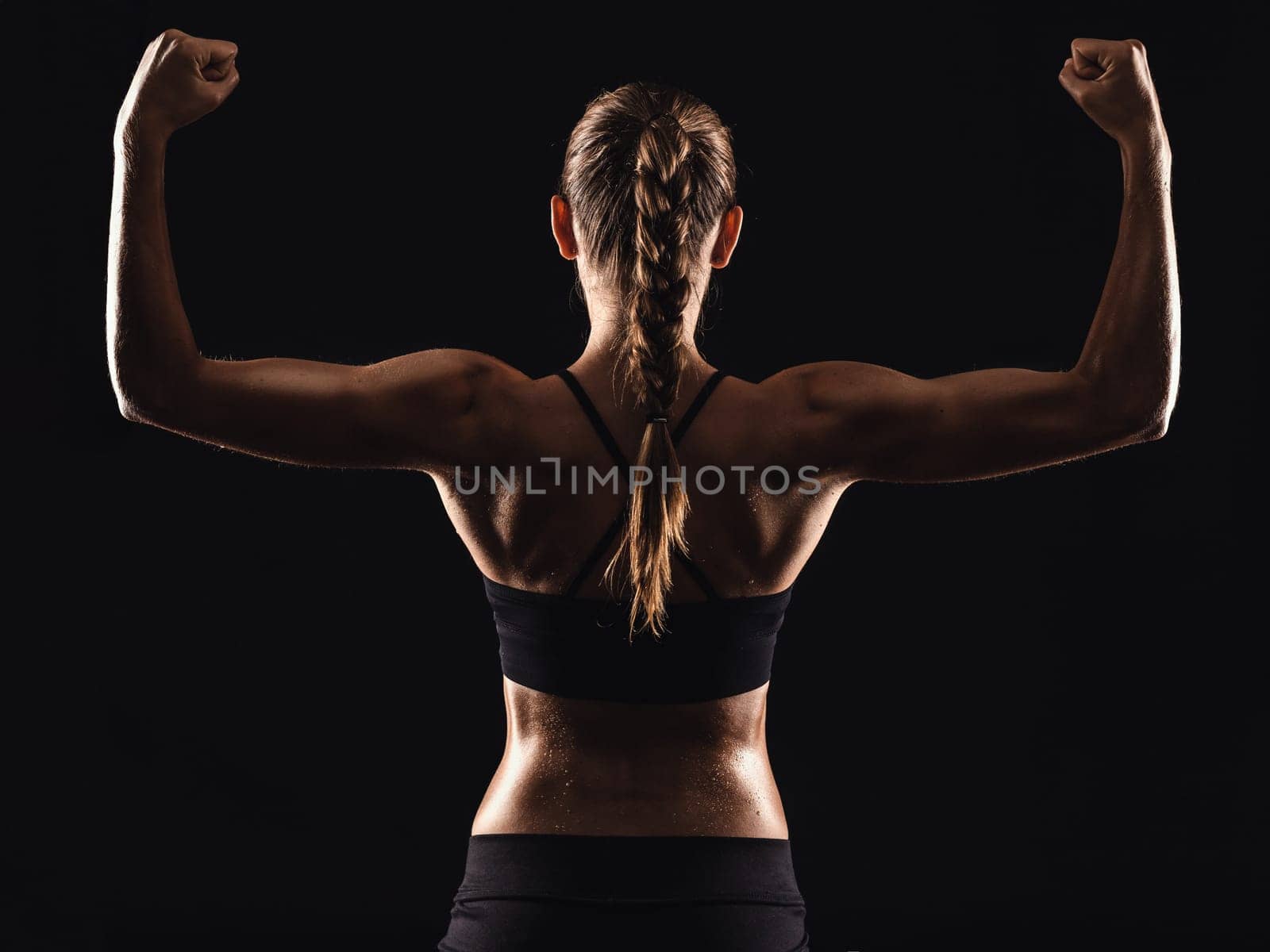 Studio shot of a fit young woman showing her muscles, against a dark background