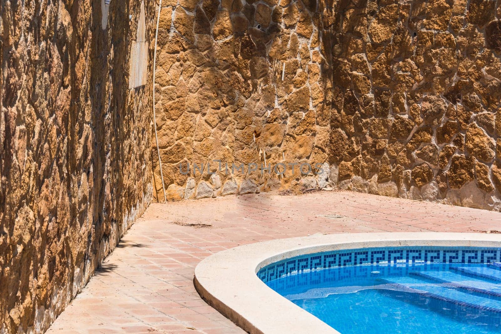Luxury swimming pool with beautiful landscaping of the territory. In the background a Mediterranean wall decorated with sandstones.