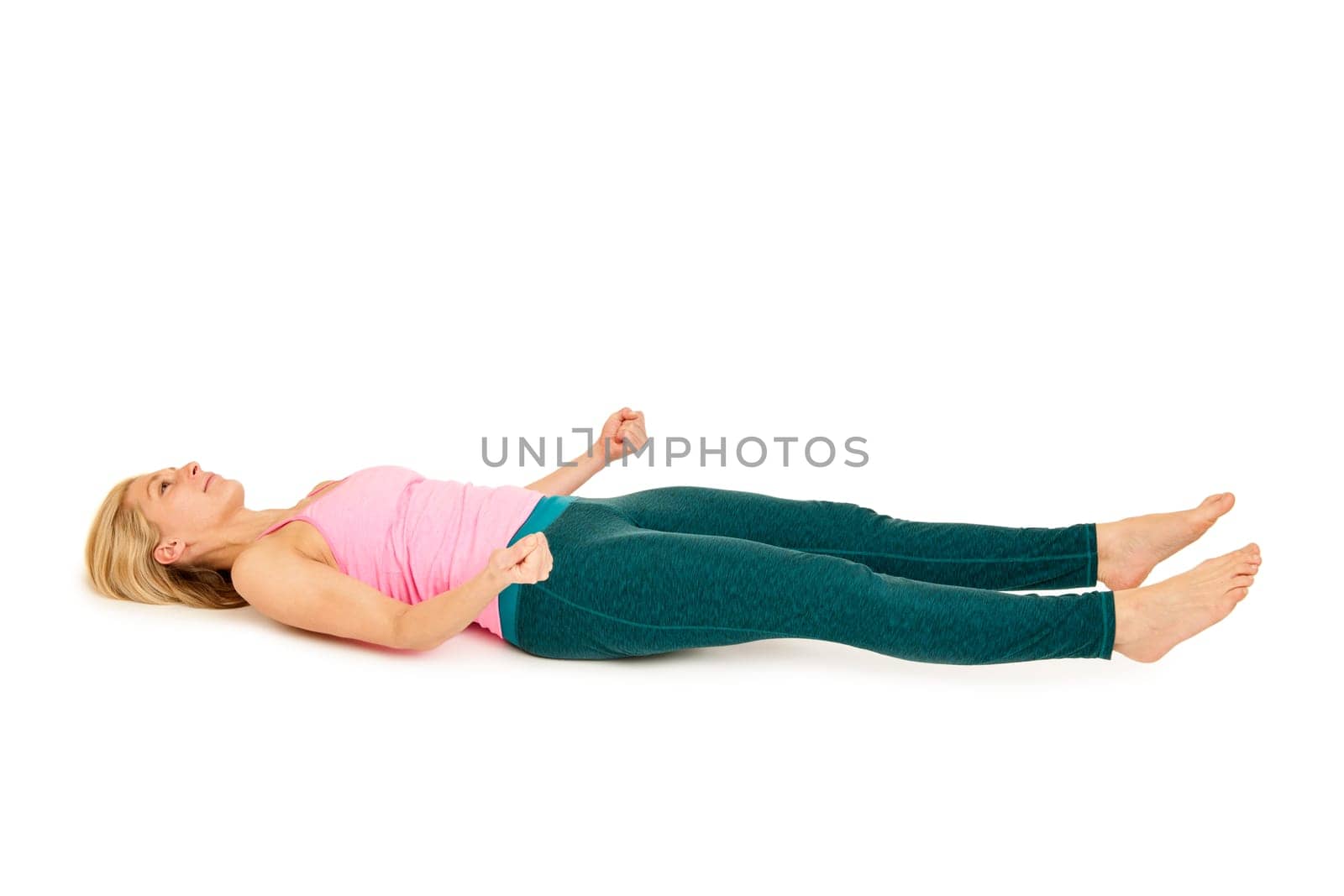 Flat-angled full-body side view of a young woman lying on her back in variation of the yoga position "totenstellung"" (shavasana) on a white background."