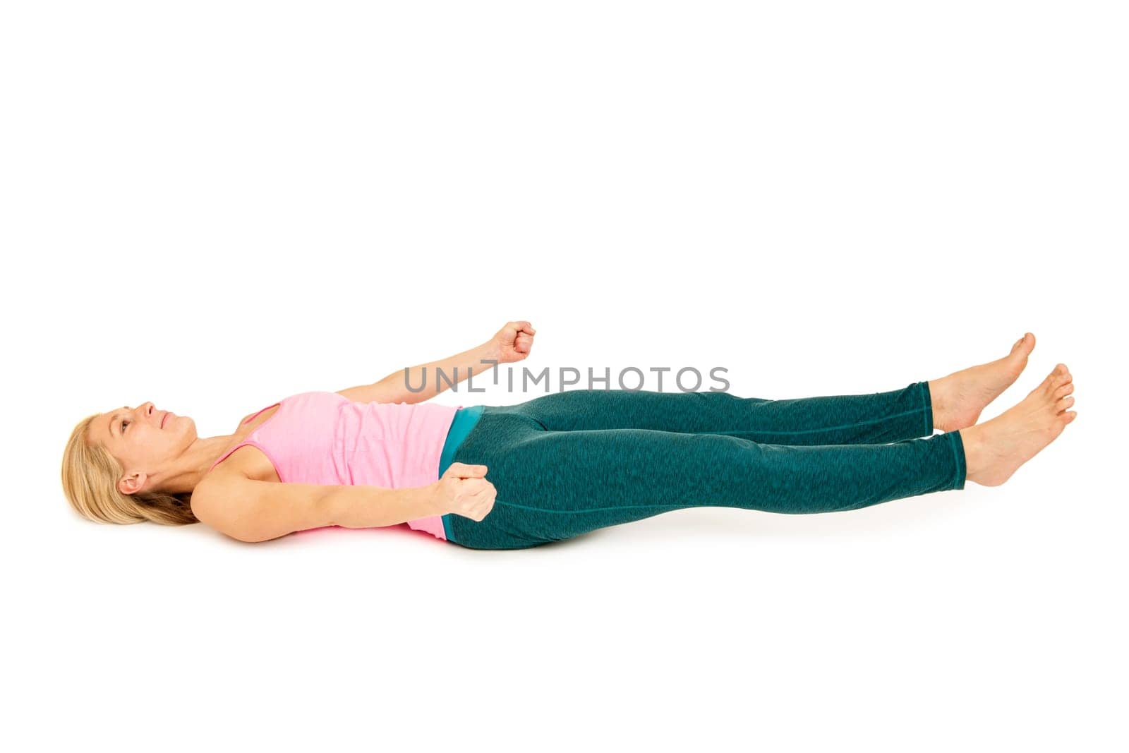 Flat-angled full-body side view of a young woman lying on her back in variation of the yoga position "totenstellung"" (shavasana) on a white background."