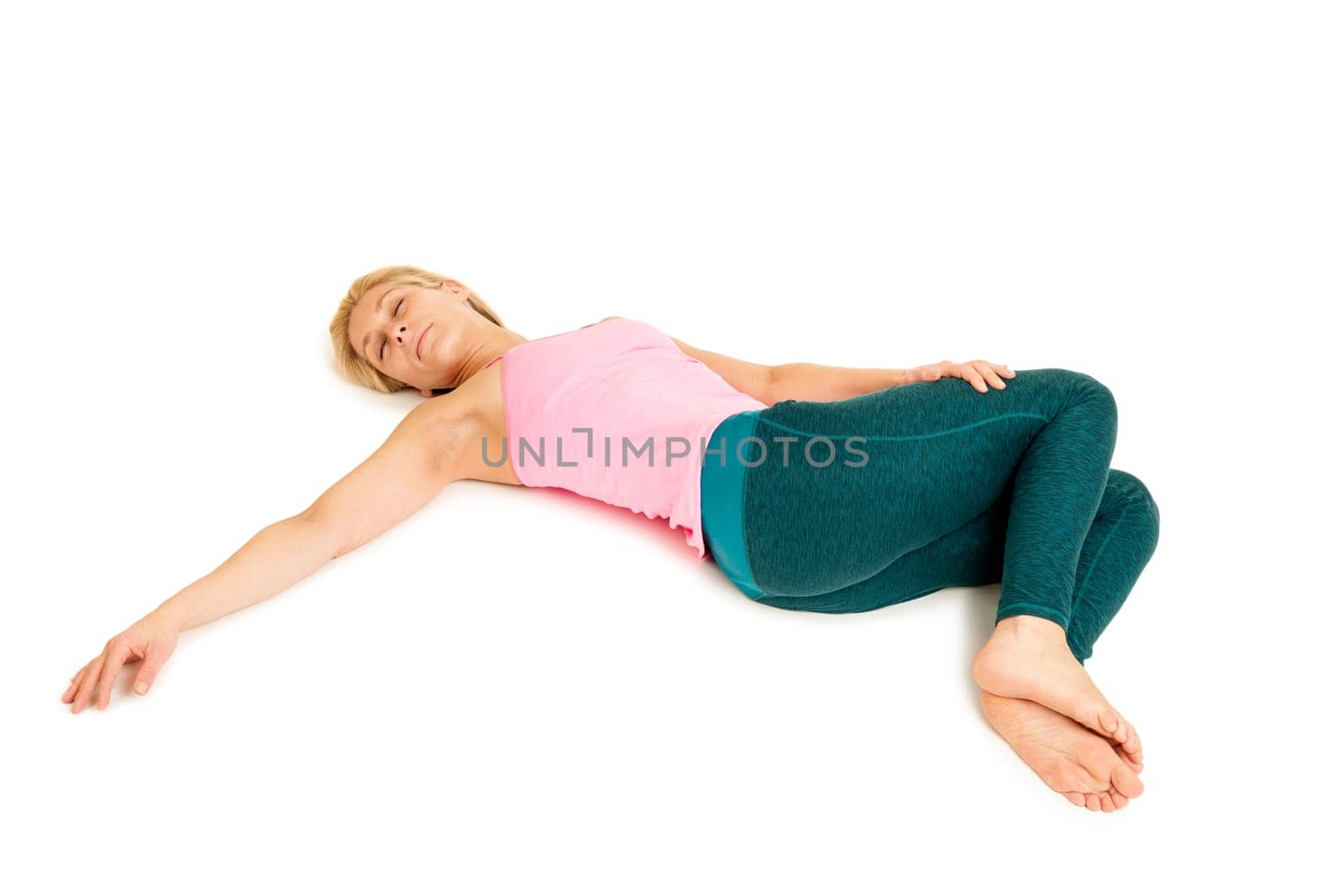 Lateral full-body view of a young woman lying on the floor in the yoga position "Crocodile"" (Nakrasana) on a white background with arms stretched out to the side."