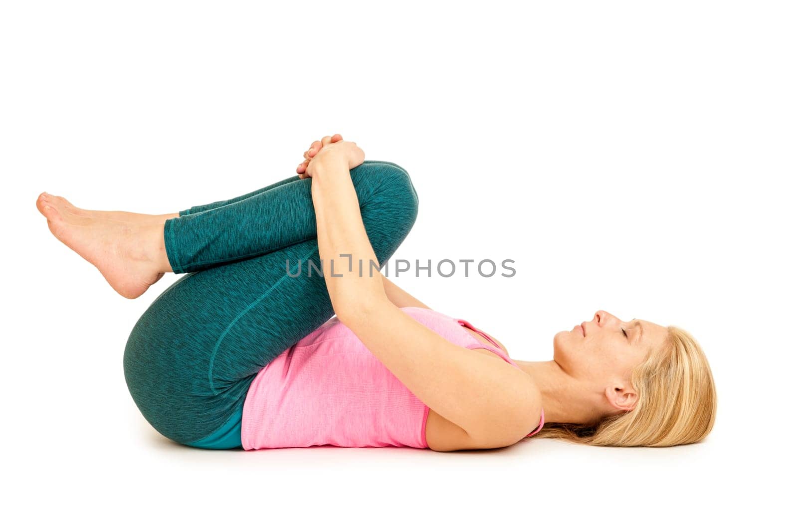 Flat-angled full-body view of a young woman lying on her back in the yoga position "happy baby"" (anada balasana) on a white background."