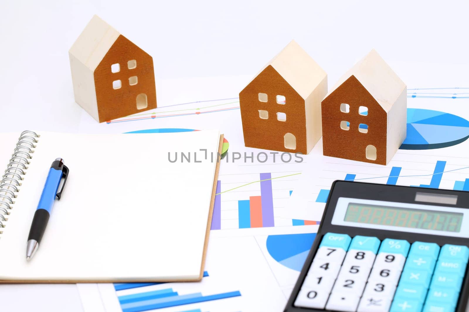 Miniature model of house on chart printed documents, leather notebook and pen
