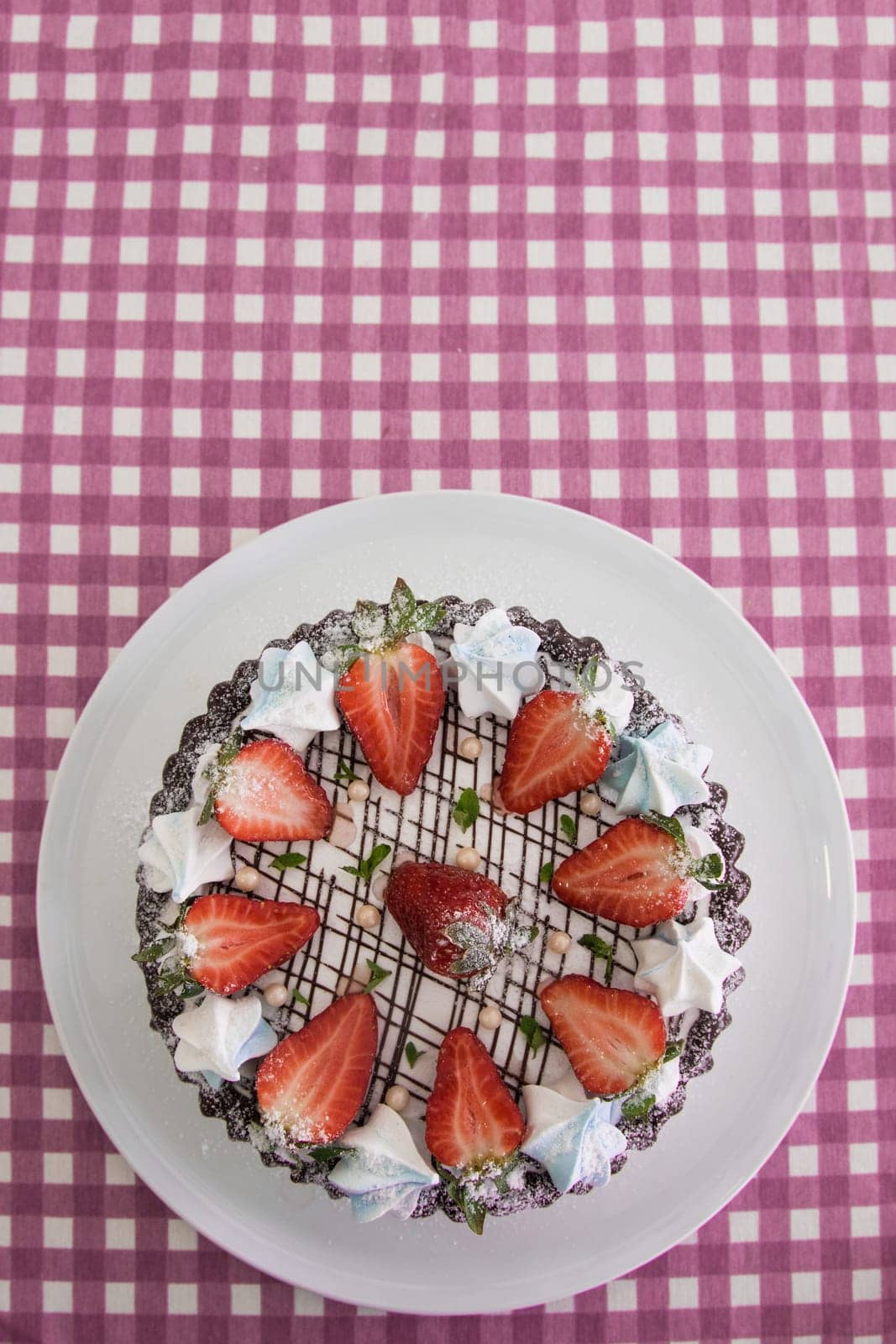 Tasty strawberry cream cake on checkered table, with tea set