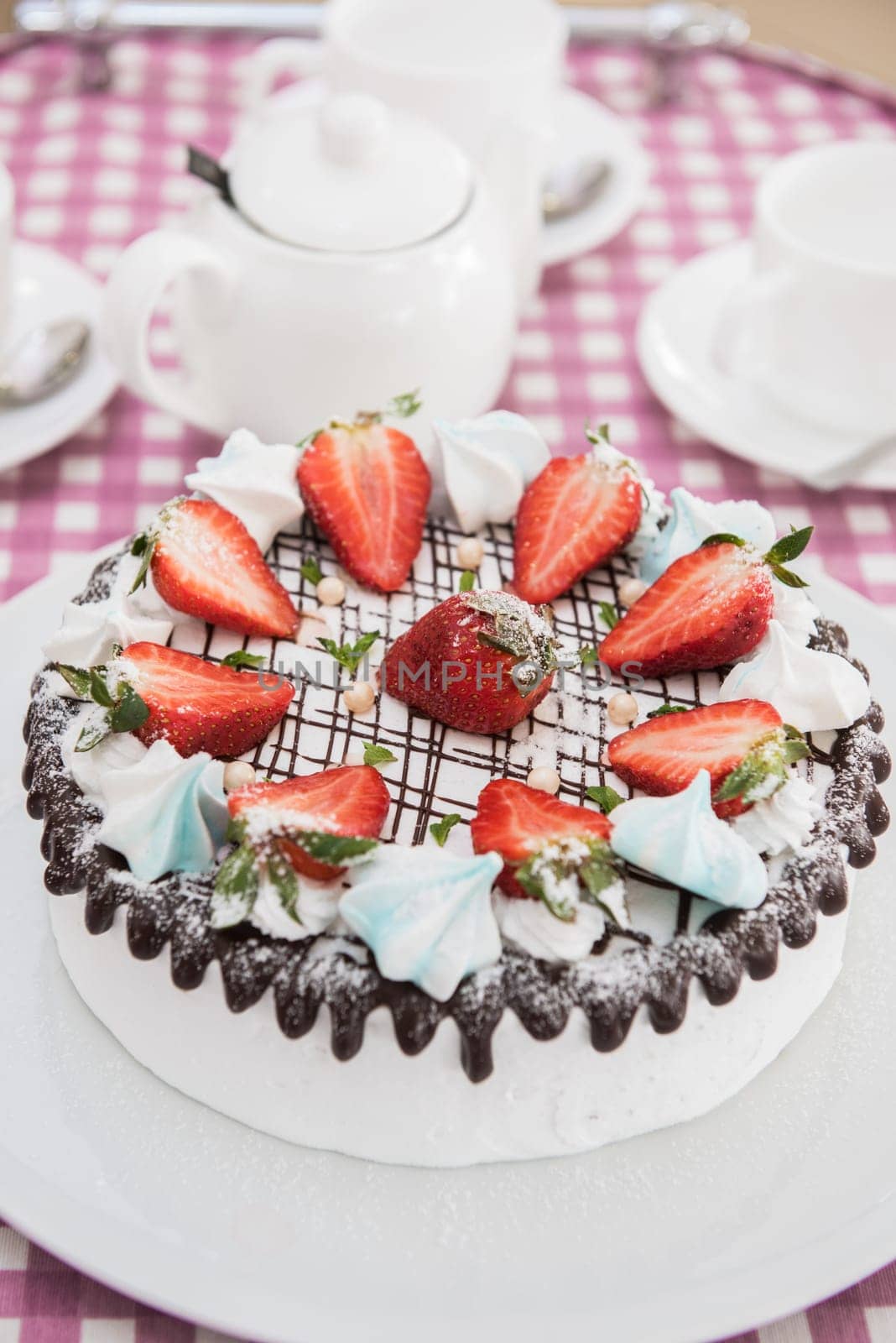 Tasty strawberry cream cake on checkered table, with tea set