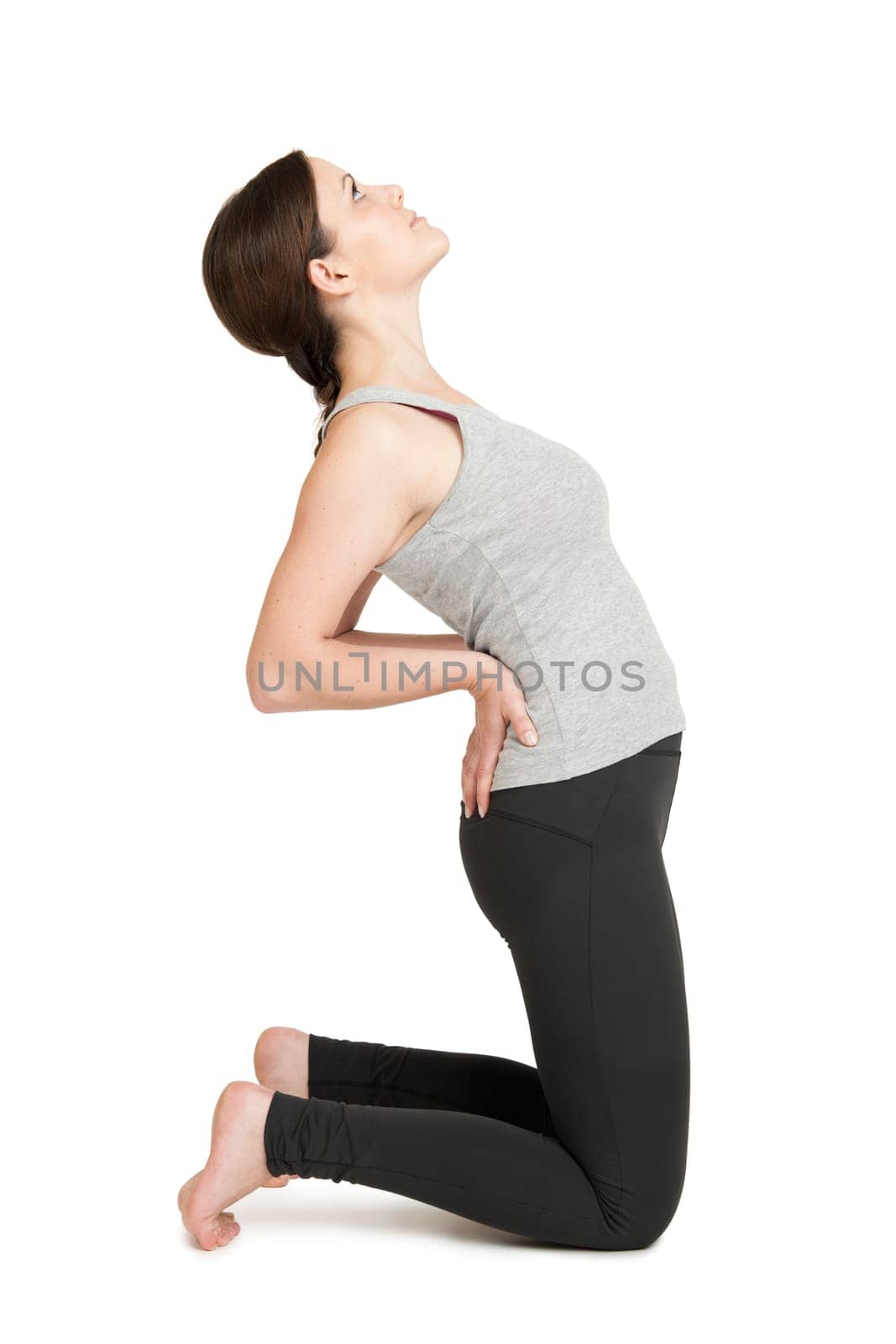 Lateral full-body view of a young woman on a white background in the knee stand,the hands supported in the hips and the upper body bent backwards. Yoga position Ustrasana,the camel  in a simplified version.