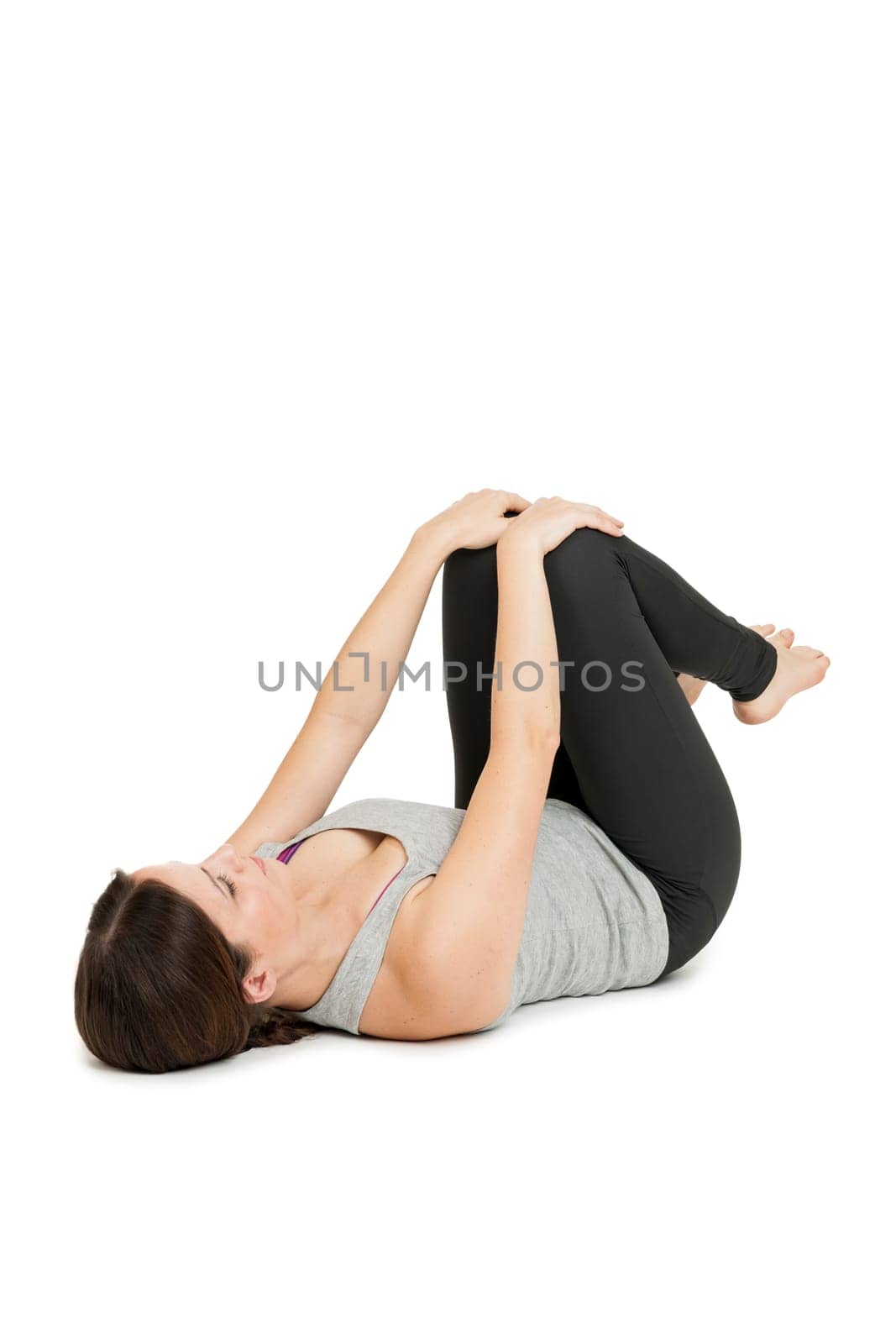 Flat-angled full-body view of a young woman lying on her back in the yoga position "happy baby"" (anada balasana) on a white background."