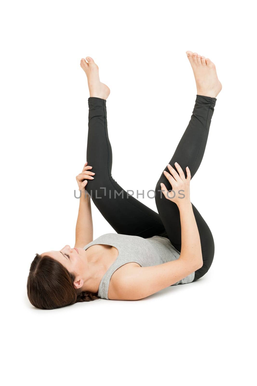 Flat-angled full-body view of a young woman lying on her back in the yoga position "happy baby"" (anada balasana) on a white background."