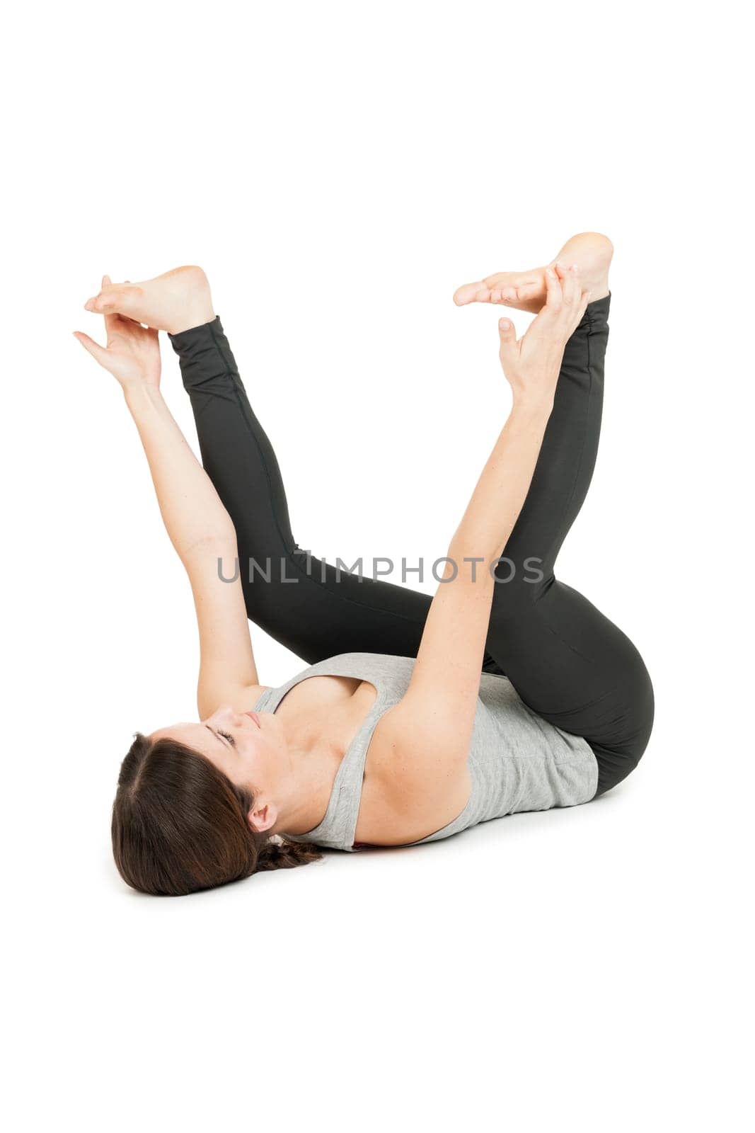 Flat-angled full-body view of a young woman lying on her back in the yoga position "happy baby"" (anada balasana) on a white background."