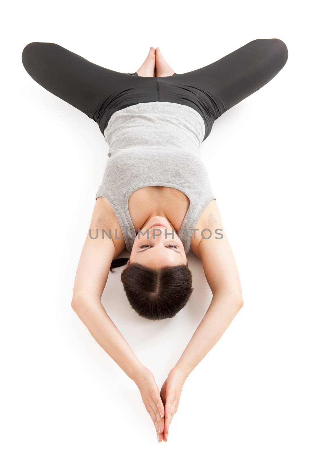 Elevated full-body view of a young woman lying on her back in the yoga position "lying butterfly"" (supta baddha konasana) on a white background."