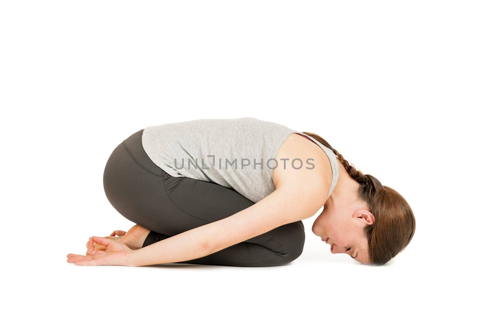 Lateral full-body view of a young woman against a white background showing the yoga figure "Position of the Child"" (Garhasana)."