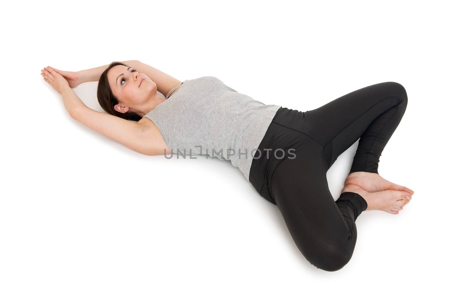 Elevated full-body view of a young woman lying on her back in the yoga position "lying butterfly"" (supta baddha konasana) on a white background."
