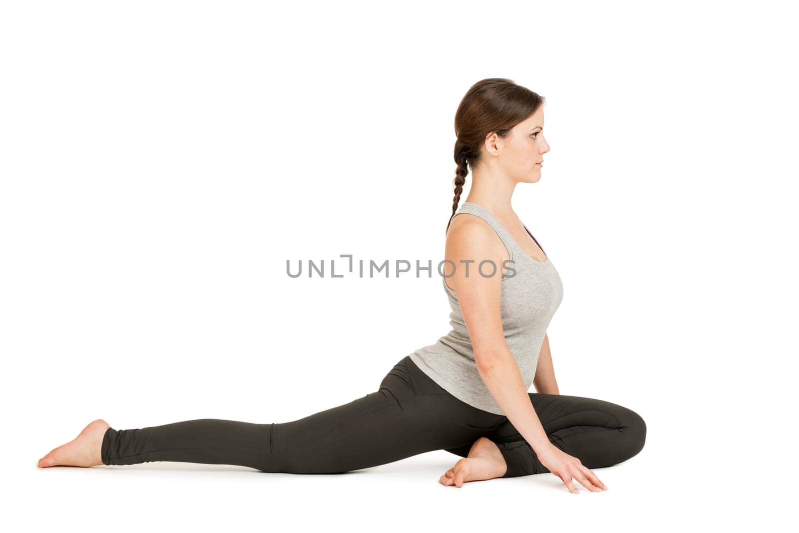 Lateral full-body view of a young woman against a white background showing the yoga exercise the dove (Eka Pada Rajakapotasana).
