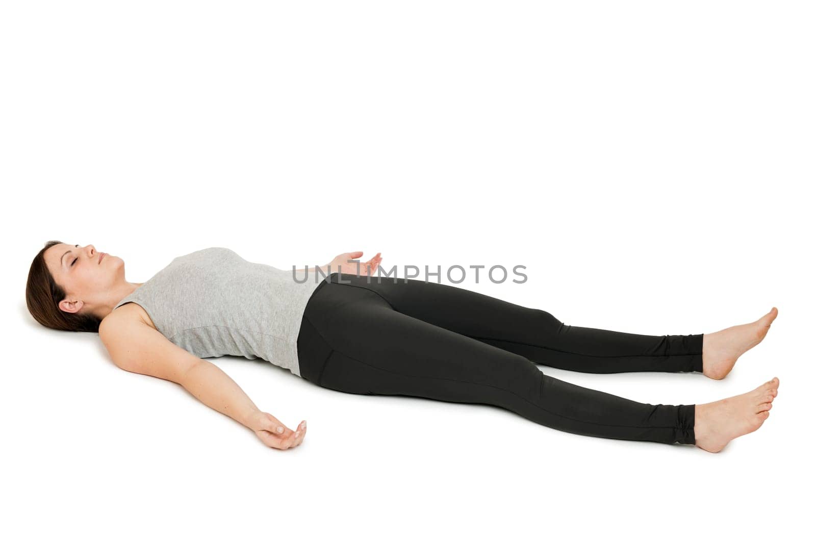 Flat-angled full-body view of a young woman lying on her back in the yoga position "Totenstellung"" (shavasana) on a white background."