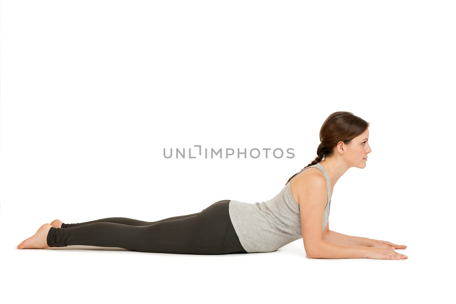 Lateral full-body view of a young woman white background showing the yoga position the Sphinx (Salamba Bhujangasana) in the basic position.