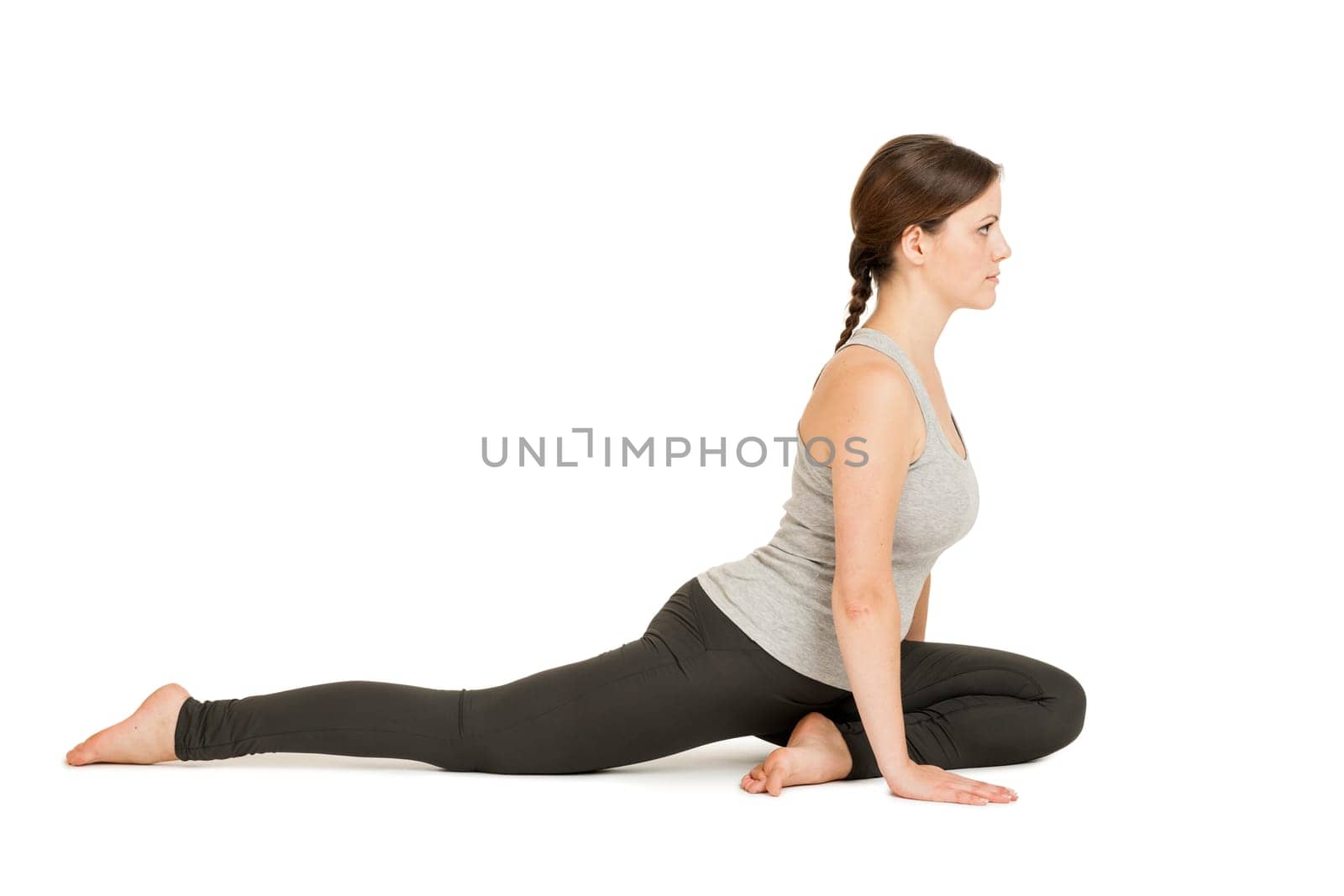 Lateral full-body view of a young woman against a white background showing the yoga exercise the dove (Eka Pada Rajakapotasana).