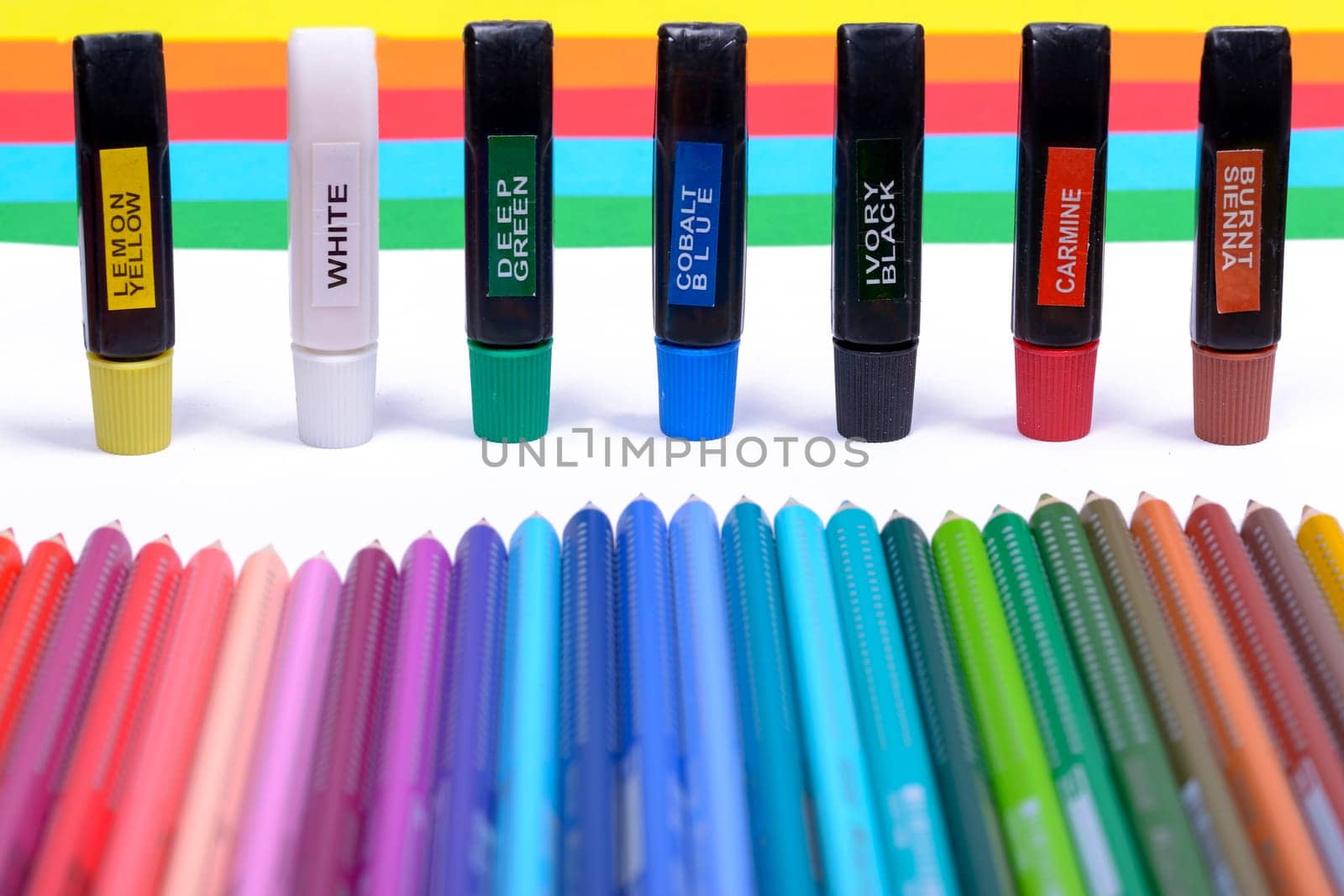 Bundle of colored pencils and tubes of paint on the colorful background