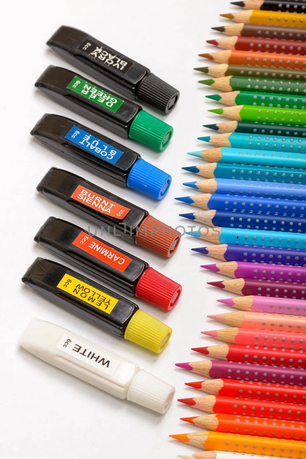 Bundle of colored pencils and tubes of paint on the colorful background