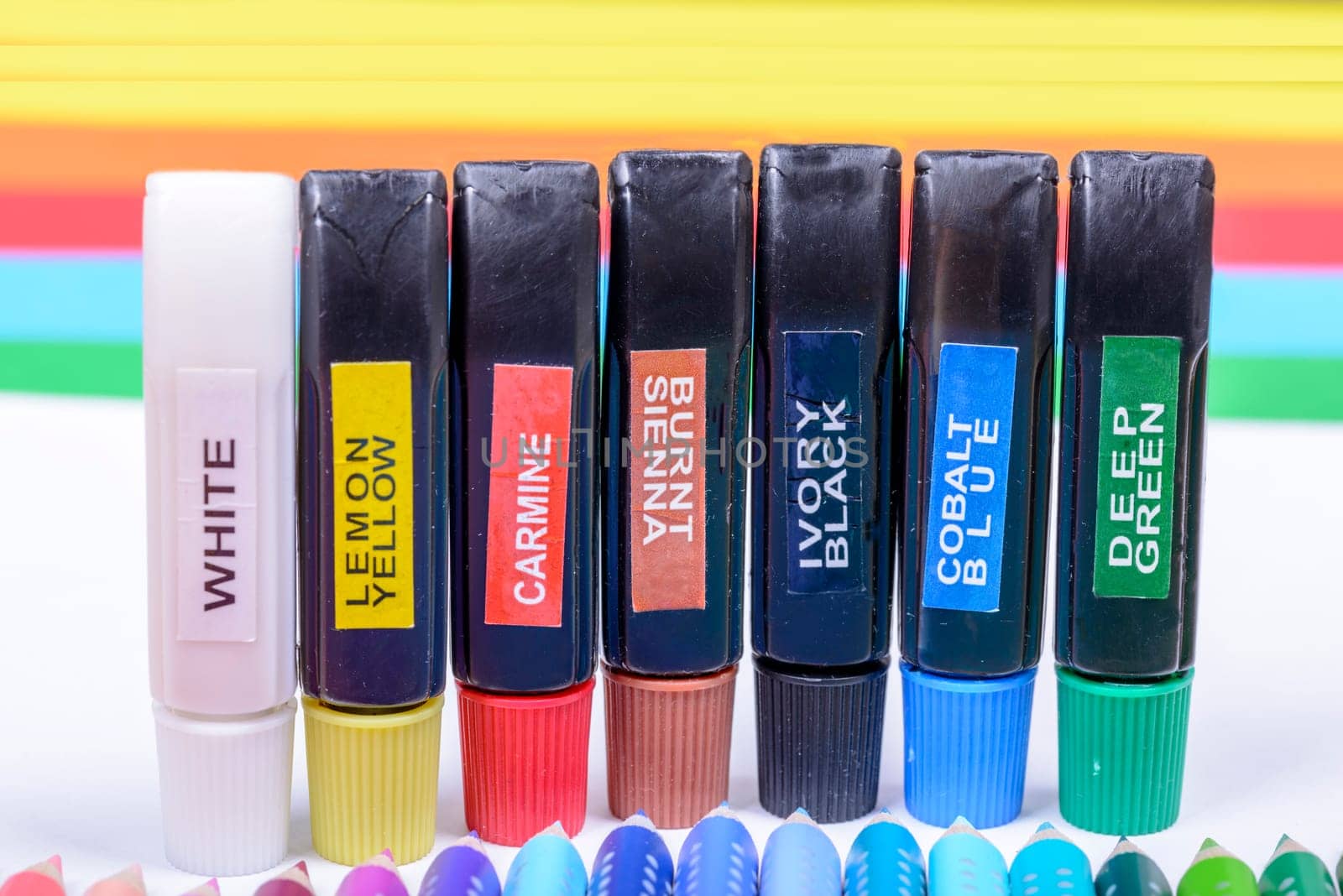 Bundle of colored pencils and tubes of paint on the colorful background