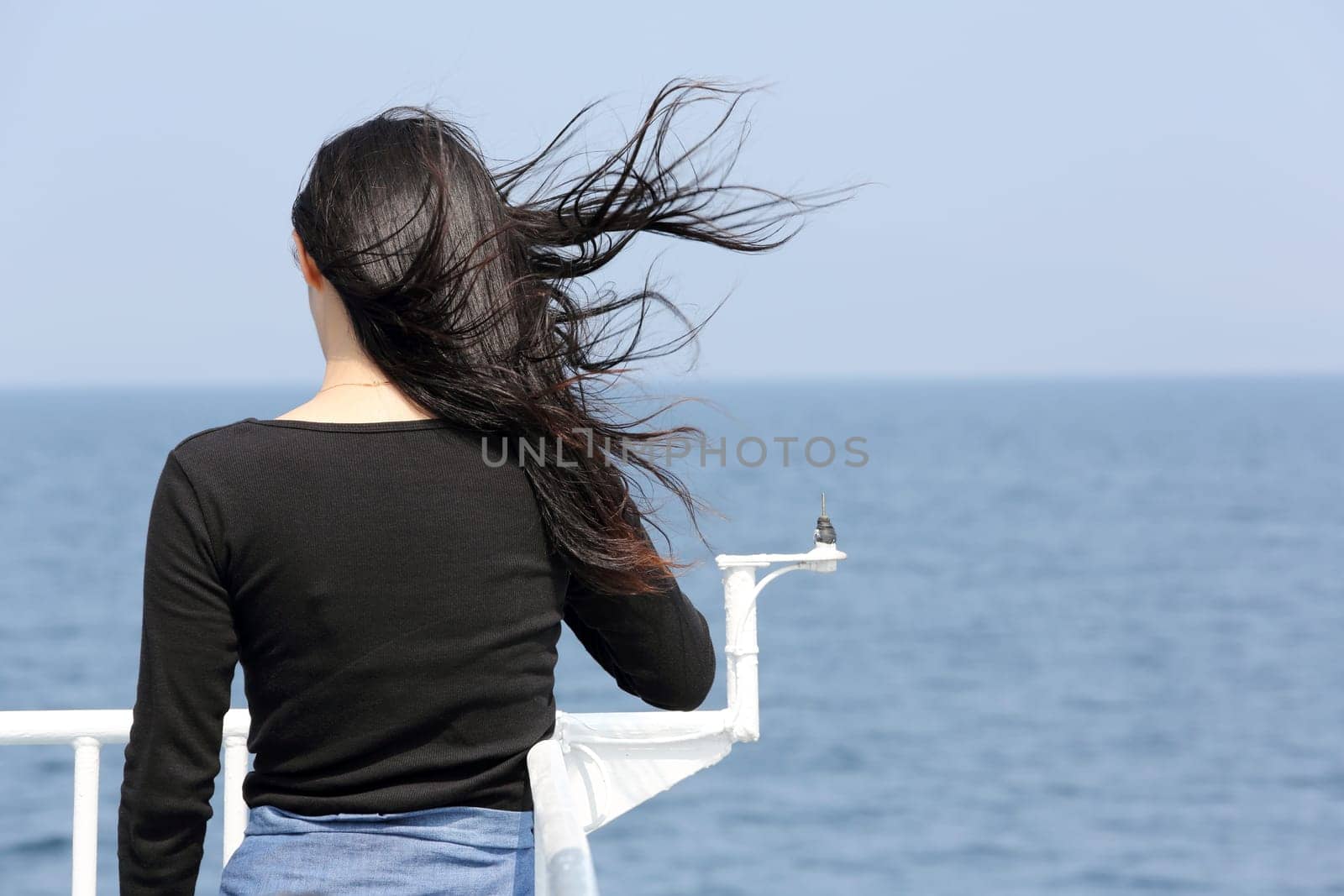 Back view of young asian woman with waving long hair from the deck of cruise ship